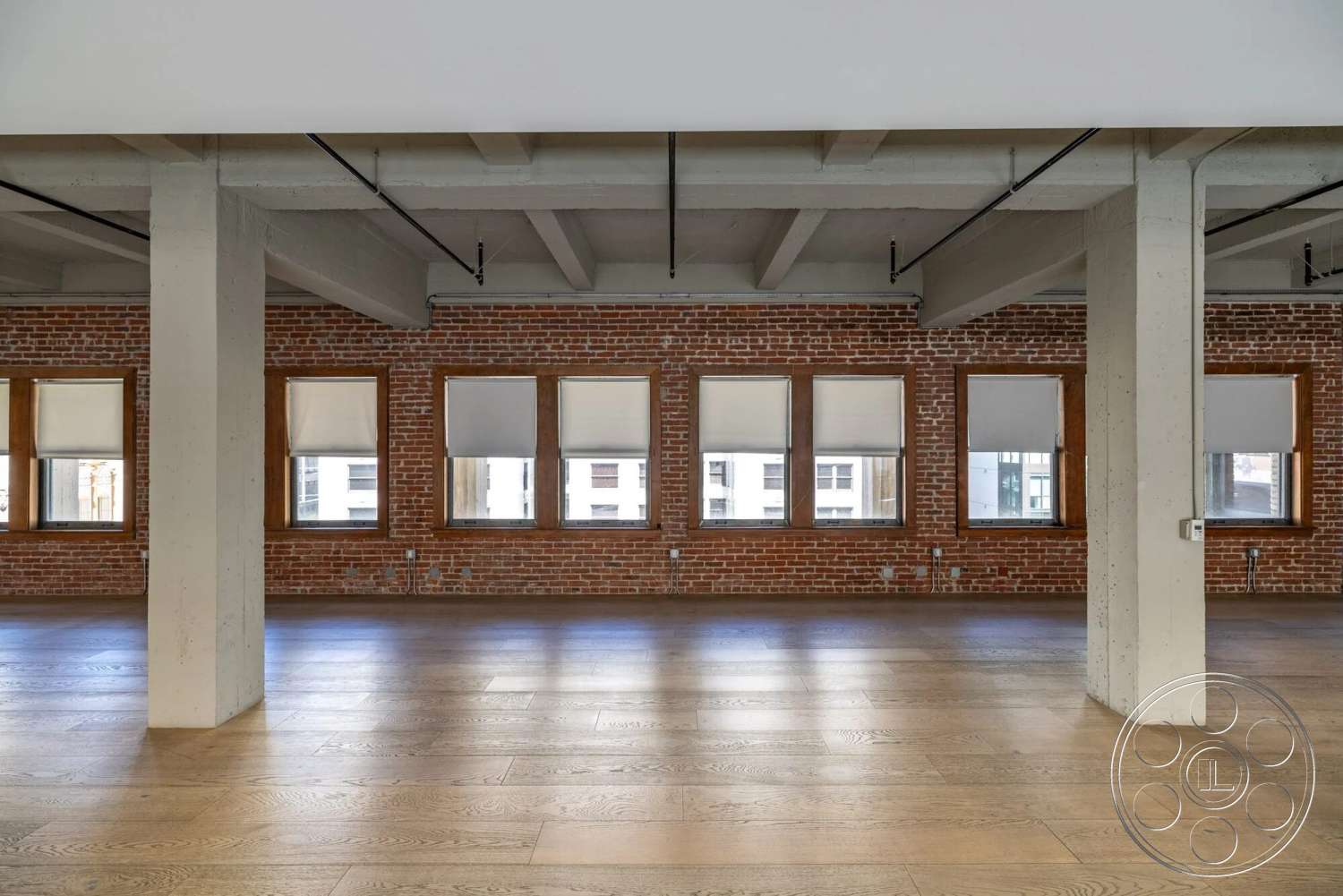 Loft 1 - light hardwood flooring, interior space, industrial style, exposed brick walls, floor-to-ceiling windows, large windows with shades, concrete ceiling beams