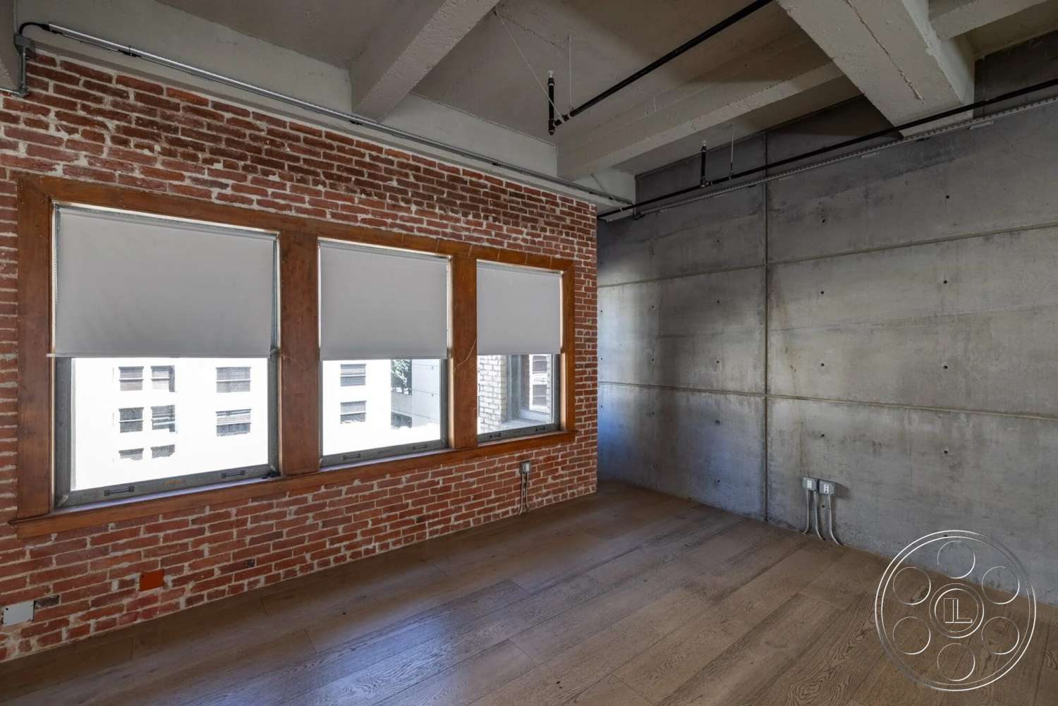 Loft 1 - large windows, natural light, hardwood flooring, open floor plan, concrete walls, metal pipes, wood window frames, exposed brick accent wall, urban loft style, industrial ceiling details