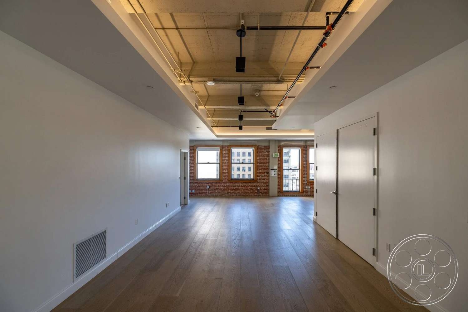 Loft 1 - open floor plan, modern interior, industrial style, floor-to-ceiling windows, hardwood floor, large doorways, white painted walls, exposed brick accent wall, natural light flooding space, floating ceiling with exposed ductwork