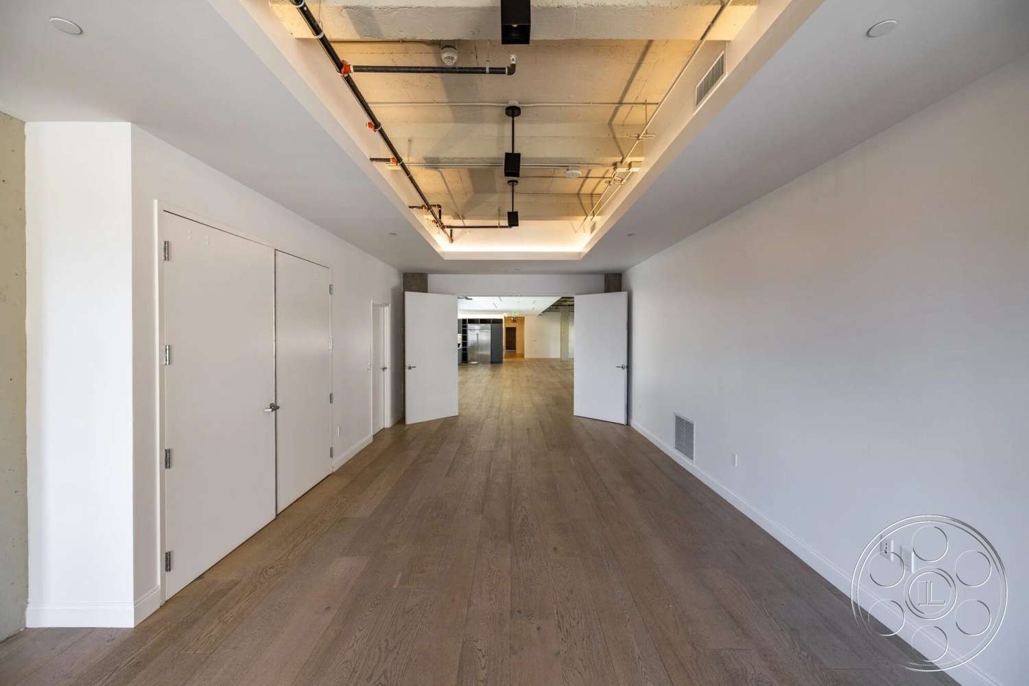 Loft 1 - minimalist design, light hardwood flooring, open floor plan, modern light fixtures, industrial elements, exposed concrete ceiling, white painted walls, straight hallway, floor-to-ceiling doors