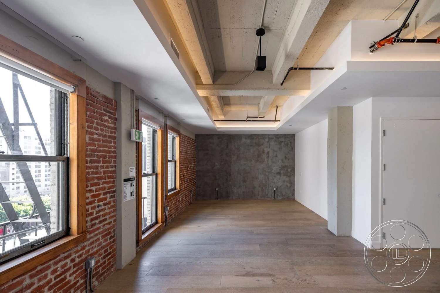 Loft 1 - hardwood flooring, open floor plan, exposed ductwork, wood beam ceiling, white painted walls, exposed brick accent wall, industrial-style lighting fixtures, steel window frames, smooth concrete feature wall