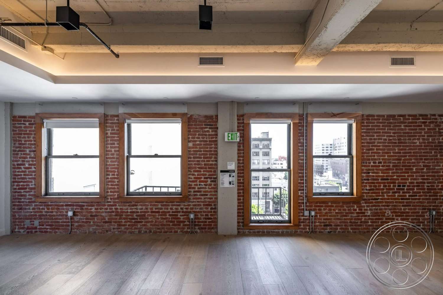 Loft 1 - natural light, hardwood flooring, minimalist design, open floor plan, modern lighting fixtures, urban setting, floor-to-ceiling windows, exposed brick accent wall, industrial style interior, concrete ceiling beams, wood trim window frames