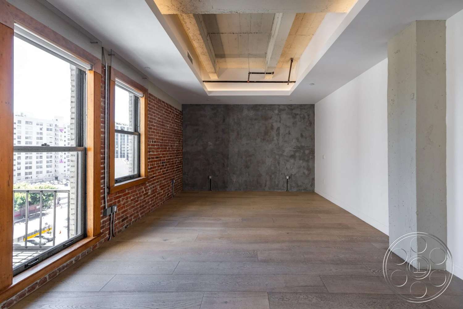 Loft 1 - hardwood flooring, open floor plan, floor-to-ceiling windows, soft ambient lighting, exposed concrete ceiling, wood window frames, concrete feature wall, exposed brick accent wall, industrial style interior, urban loft setting