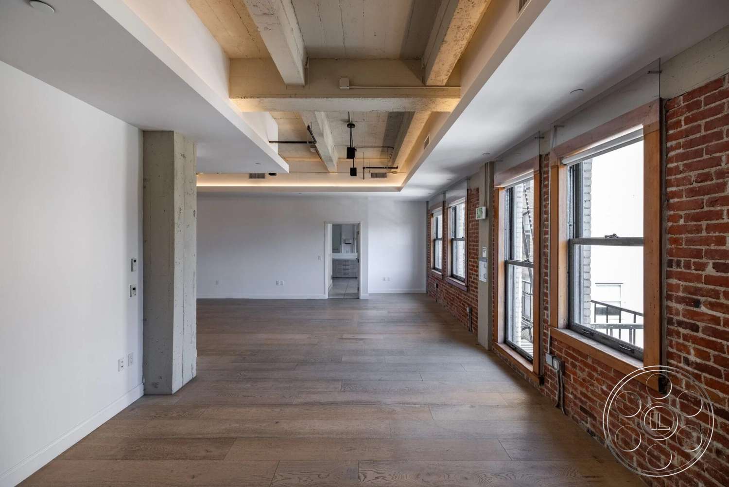 Loft 1 - neutral color palette, natural light, open floor plan, modern lighting fixtures, floor-to-ceiling windows, white painted walls, exposed brick accent wall, light wood plank flooring, industrial interior, concrete ceiling beams