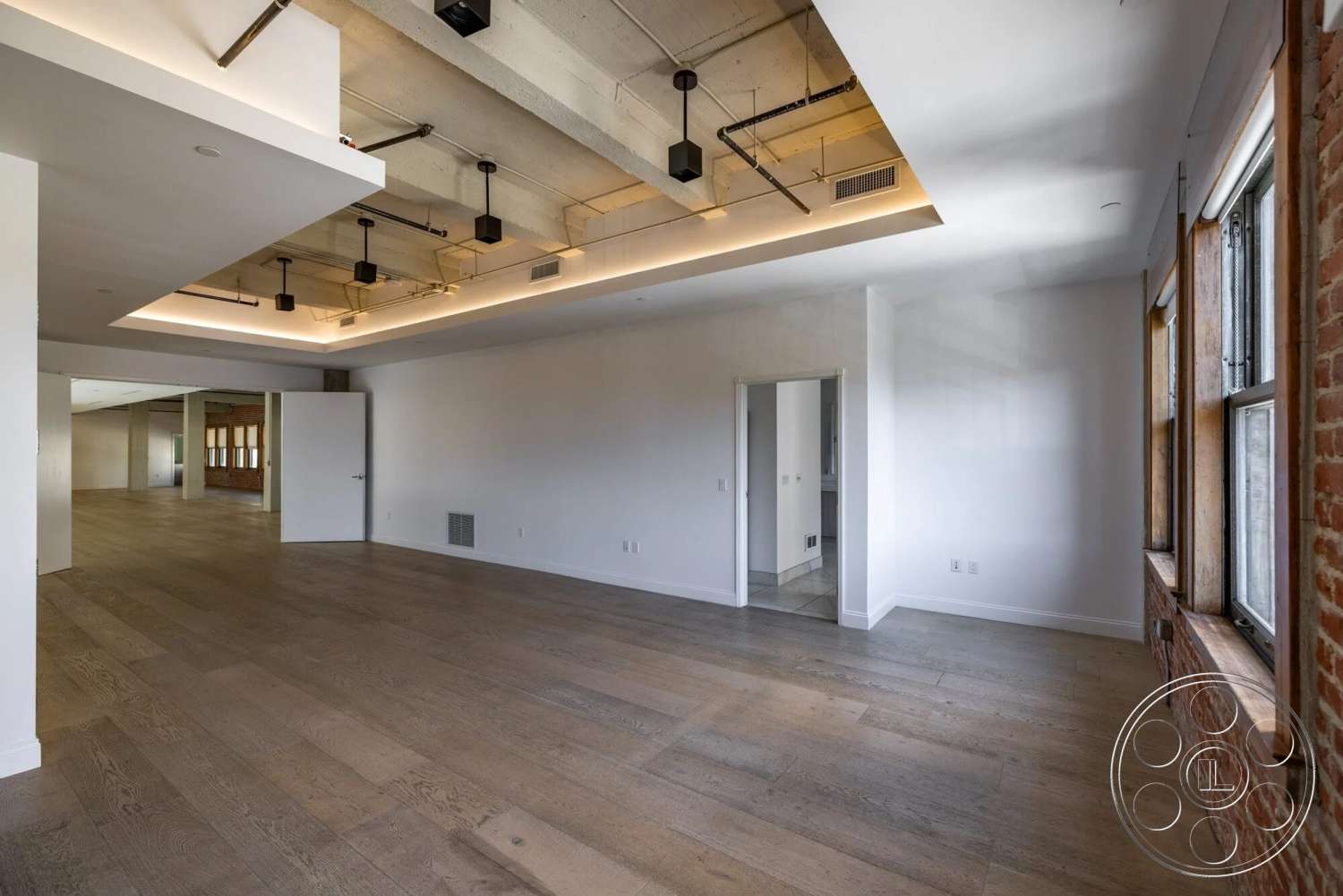 Loft 1 - large windows, hardwood flooring, recessed lighting, open floor plan, industrial style, brick accent wall, exposed concrete ceiling, white painted walls, minimalist interior, floating ceiling with LED strip lighting
