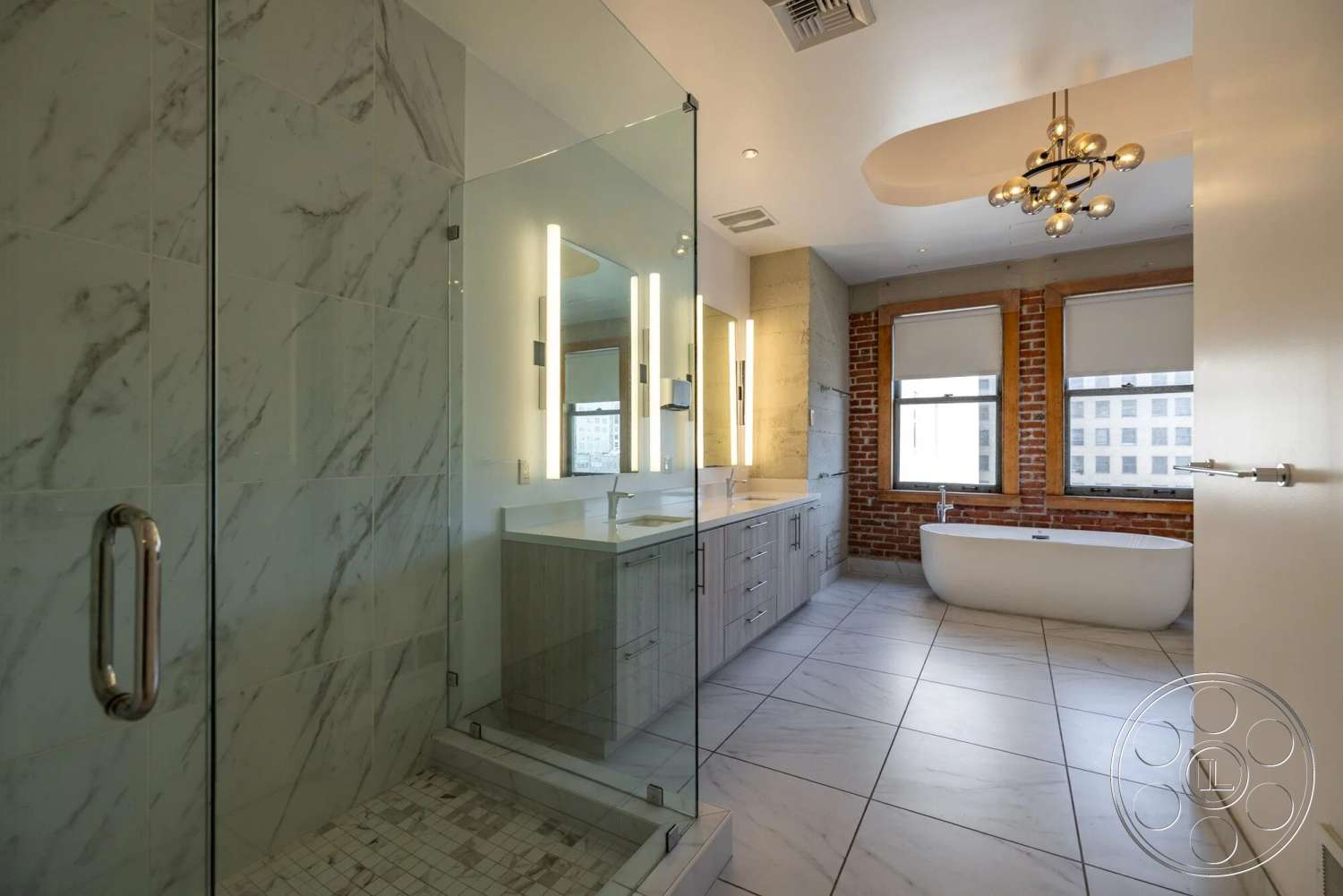 Loft 1 - large windows, contemporary design, freestanding bathtub, glass shower enclosure, double sink vanity, exposed brick accent wall, modern chandelier lighting, marble shower walls, marble tile flooring, wood vanity cabinets, mosaic tile shower floor
