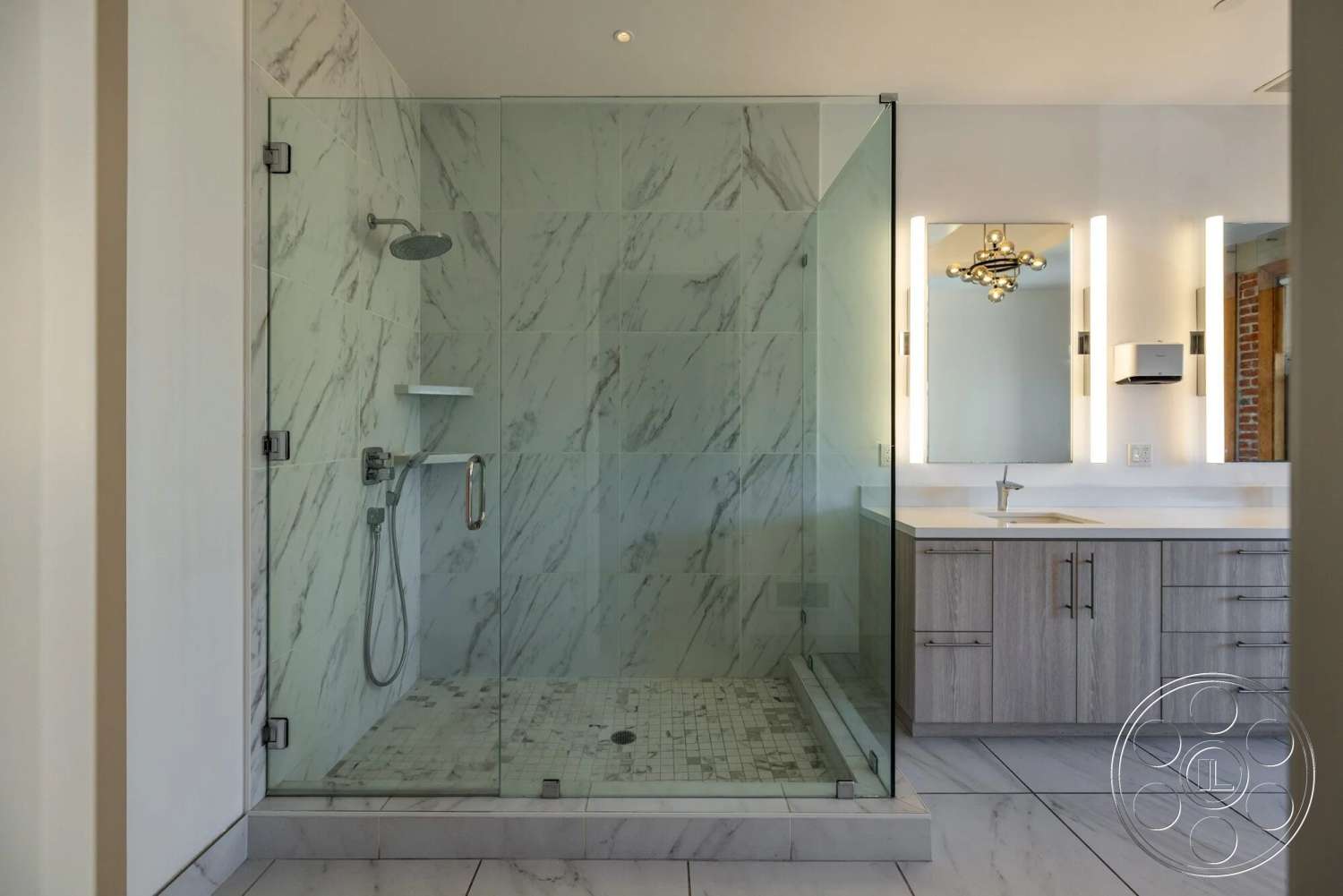 Loft 1 - tile flooring, glass shower enclosure, white quartz countertop, rain shower head, rectangular bathroom mirror, marble shower walls, marble shower floor, floating vanity with gray wood cabinets, vanity light fixtures, textured wall with exposed brick, square floor tiles