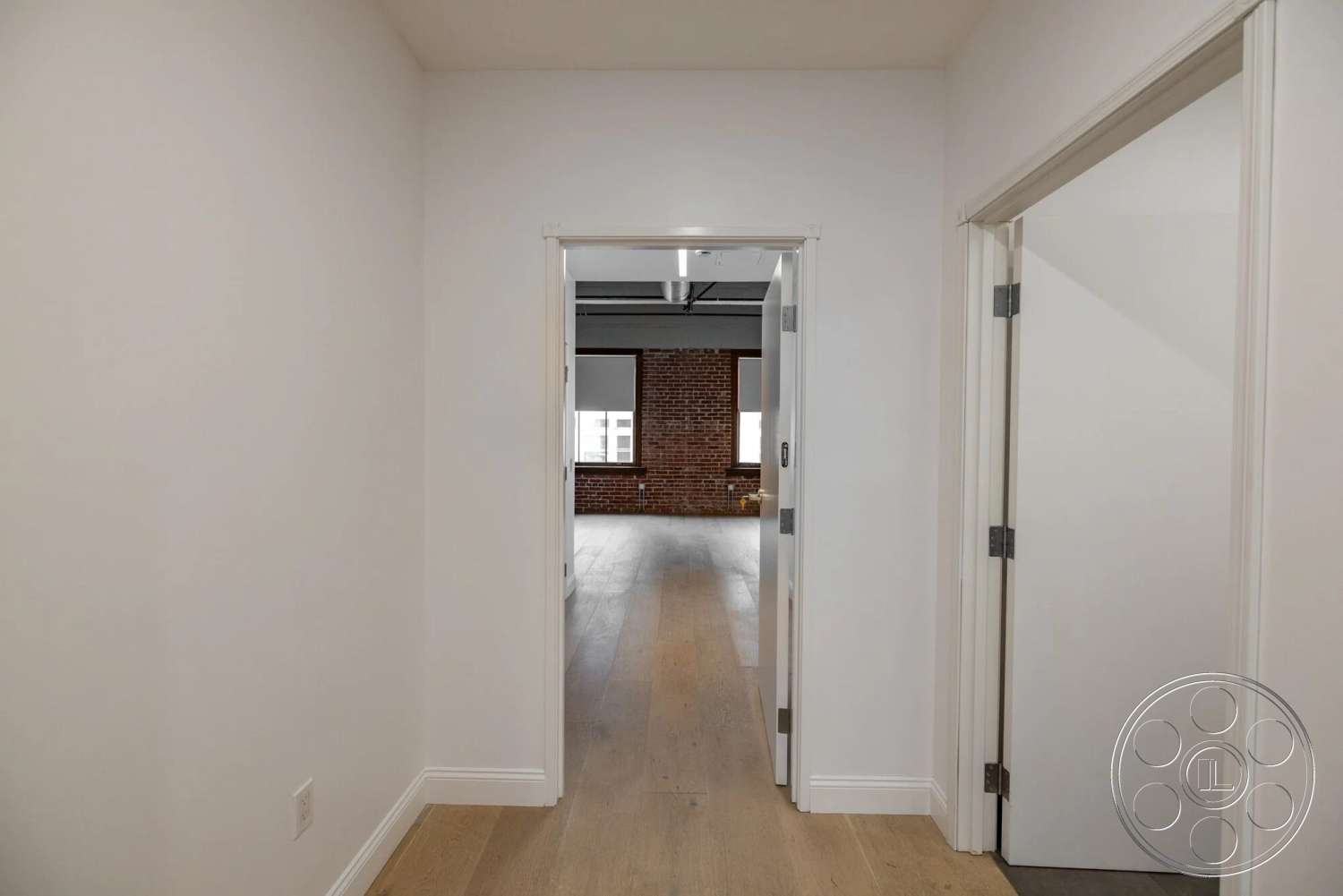 Loft 1 - open layout, floor-to-ceiling windows, white painted walls, minimalist architectural style, exposed brick accent wall, light hardwood hallway floors, modern door frames