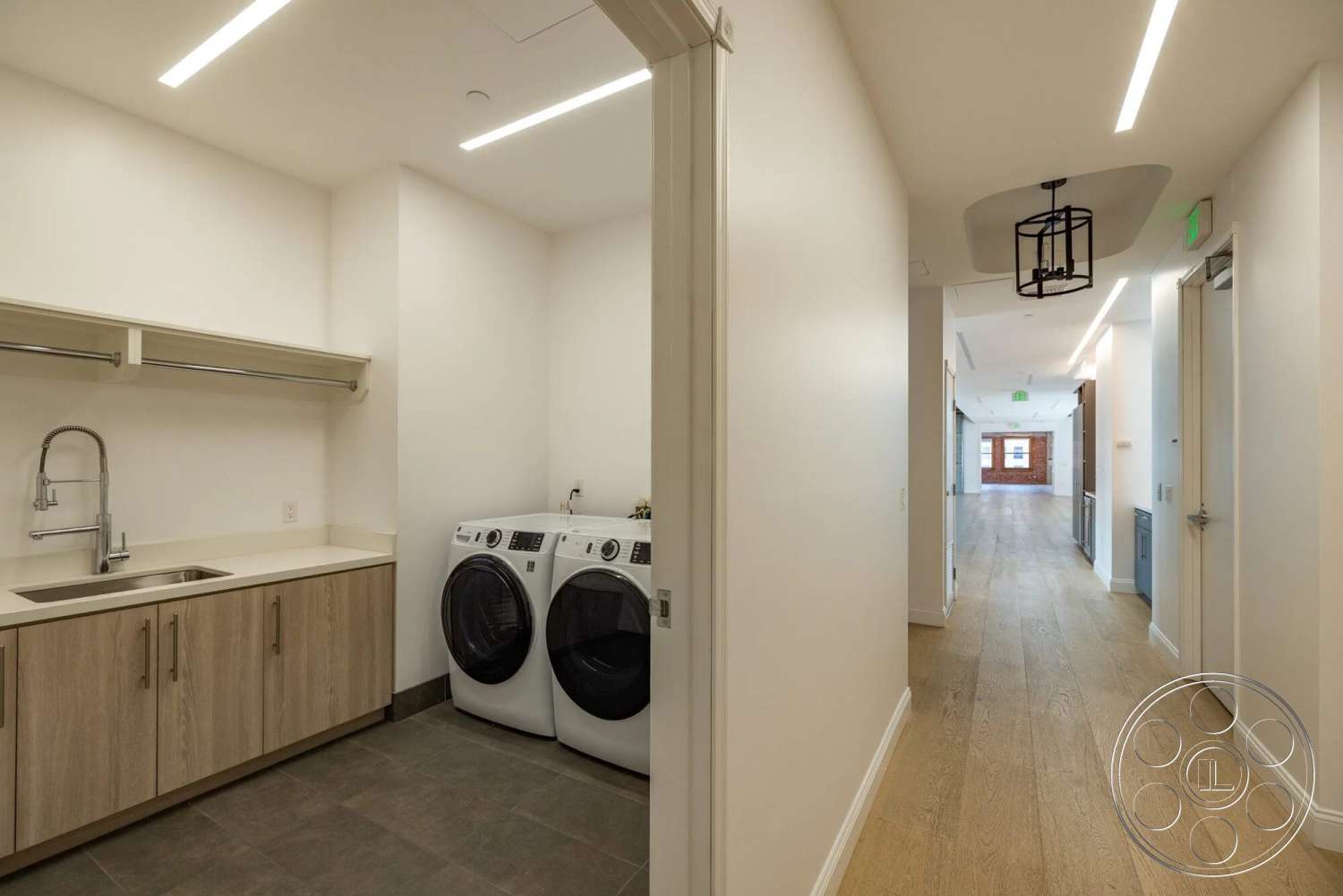 Loft 1 - natural light, open shelving, laundry room, modern light fixtures, long hallway, light wood cabinetry, gray tile flooring, stainless steel sink, white painted walls, wide plank hardwood flooring, washer and dryer units, floating ceiling design
