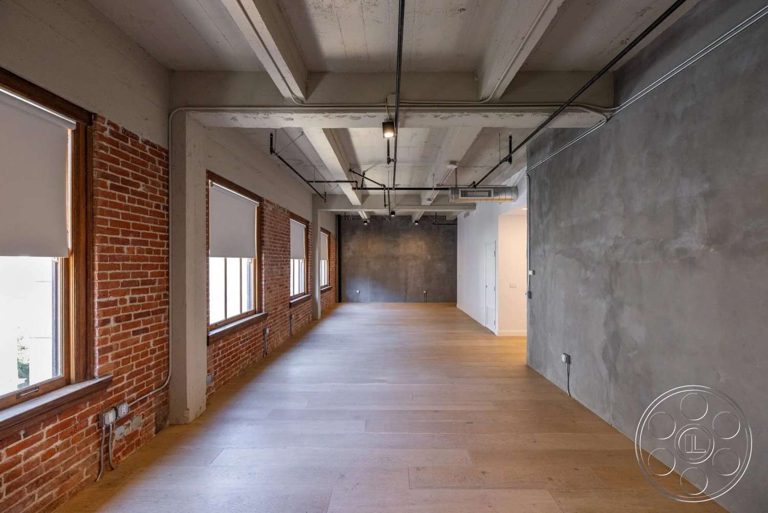 Loft 1 - high ceilings, natural light, light hardwood flooring, open floor plan, modern lighting fixtures, urban loft, exposed ductwork, concrete ceilings, exposed brick accent wall, minimalist interior, industrial style windows, polished concrete wall
