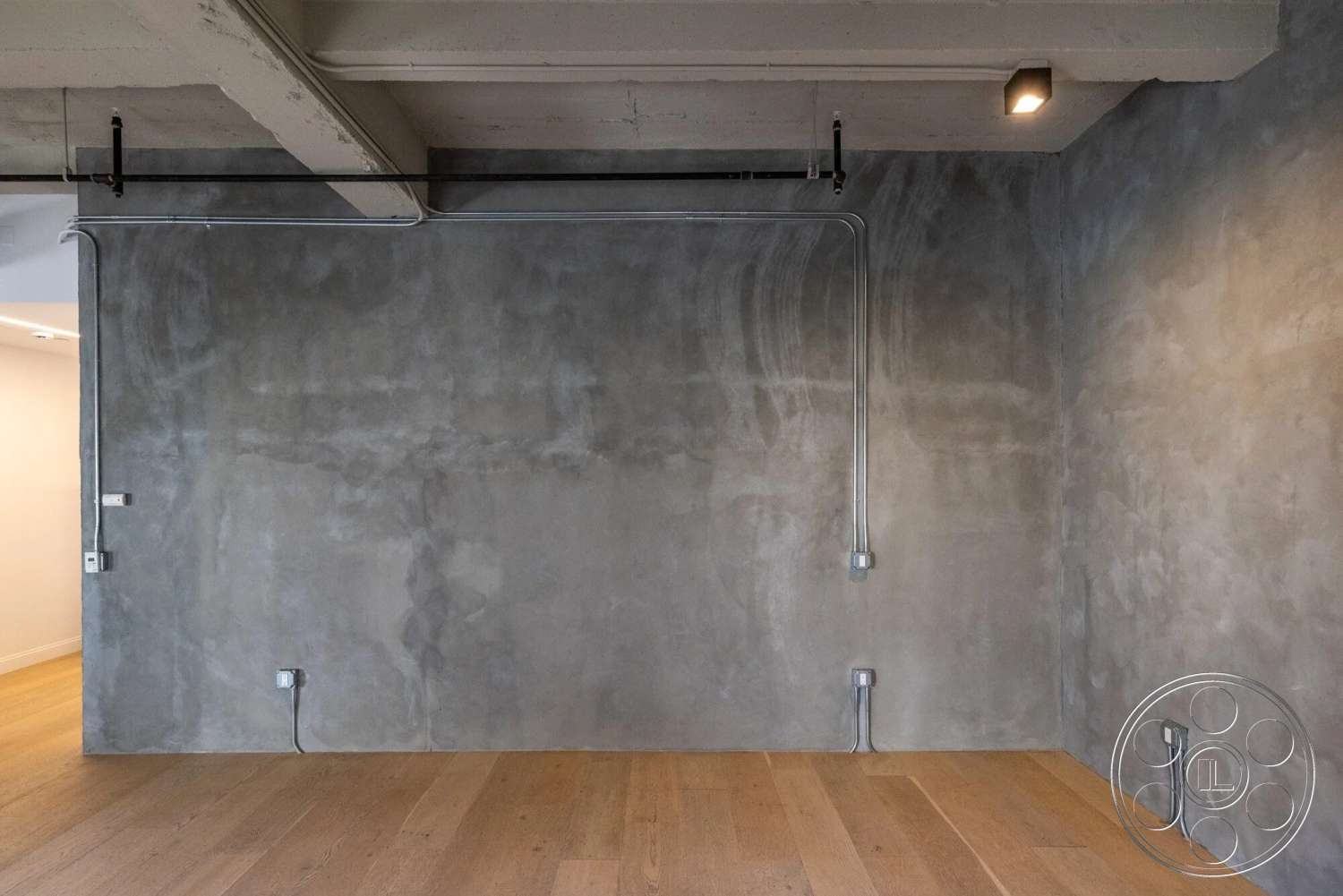 Loft 1 - exposed concrete wall, minimalist interior, wood plank flooring, industrial ceiling beams, light gray concrete texture, metal conduit piping