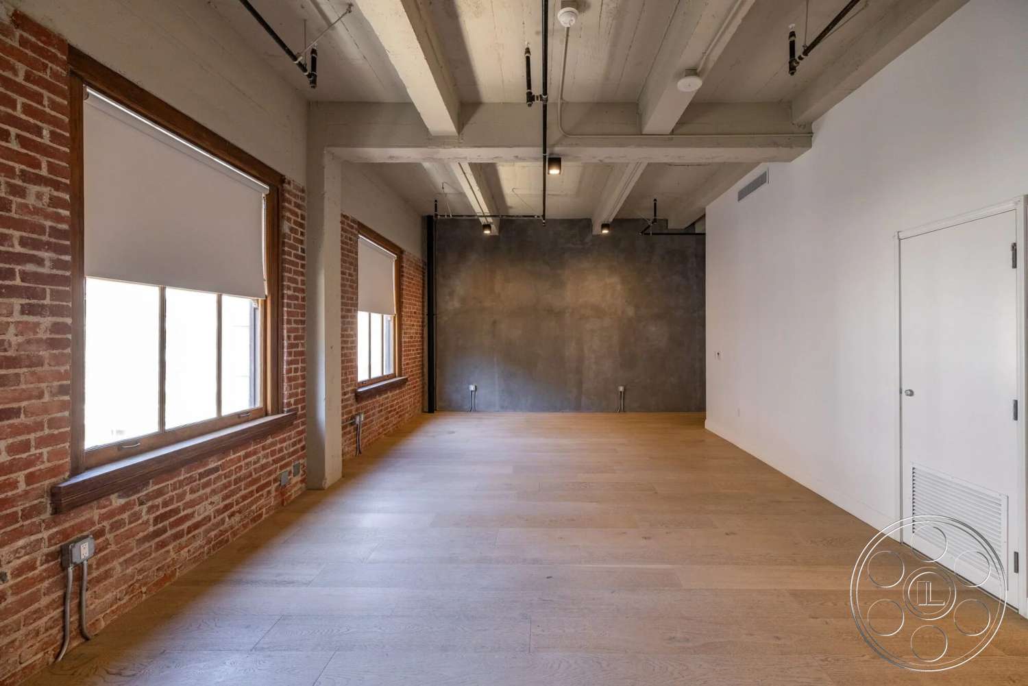 Loft 1 - neutral color palette, concrete wall, modern minimalist design, open floor plan interior, exposed brick accent wall, large windows with wooden frames, reinforced concrete ceiling, finished hardwood flooring, industrial ceiling lighting fixtures