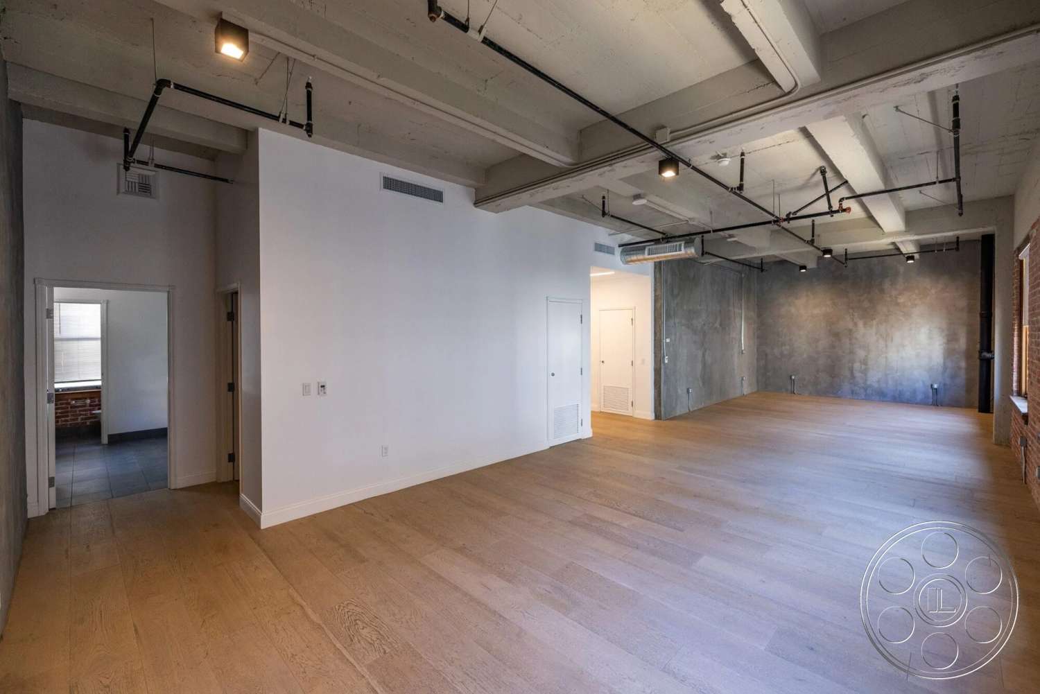 Loft 1 - large windows, wood flooring, open floor plan, modern aesthetic, exposed concrete ceiling, textured plaster wall, white painted walls, industrial-style lighting, brick wall accent