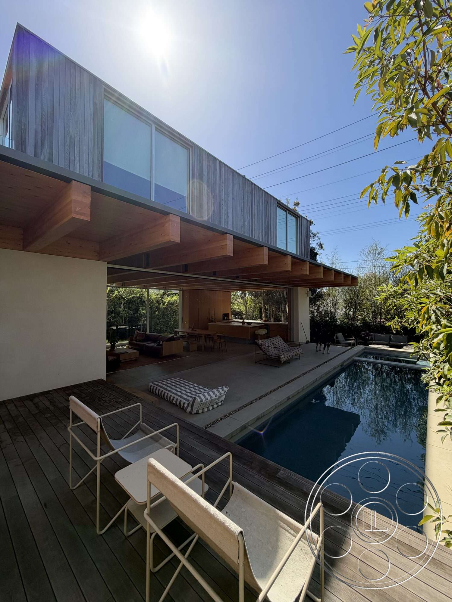 Retro House - exterior, outdoor lounge area, modern architectural style, open living space, infinity pool, stainless steel railing, vertical wood siding, sunny outdoor setting, flat roof design, wooden deck flooring, wood beam ceiling, concrete pool border, full-height glass windows