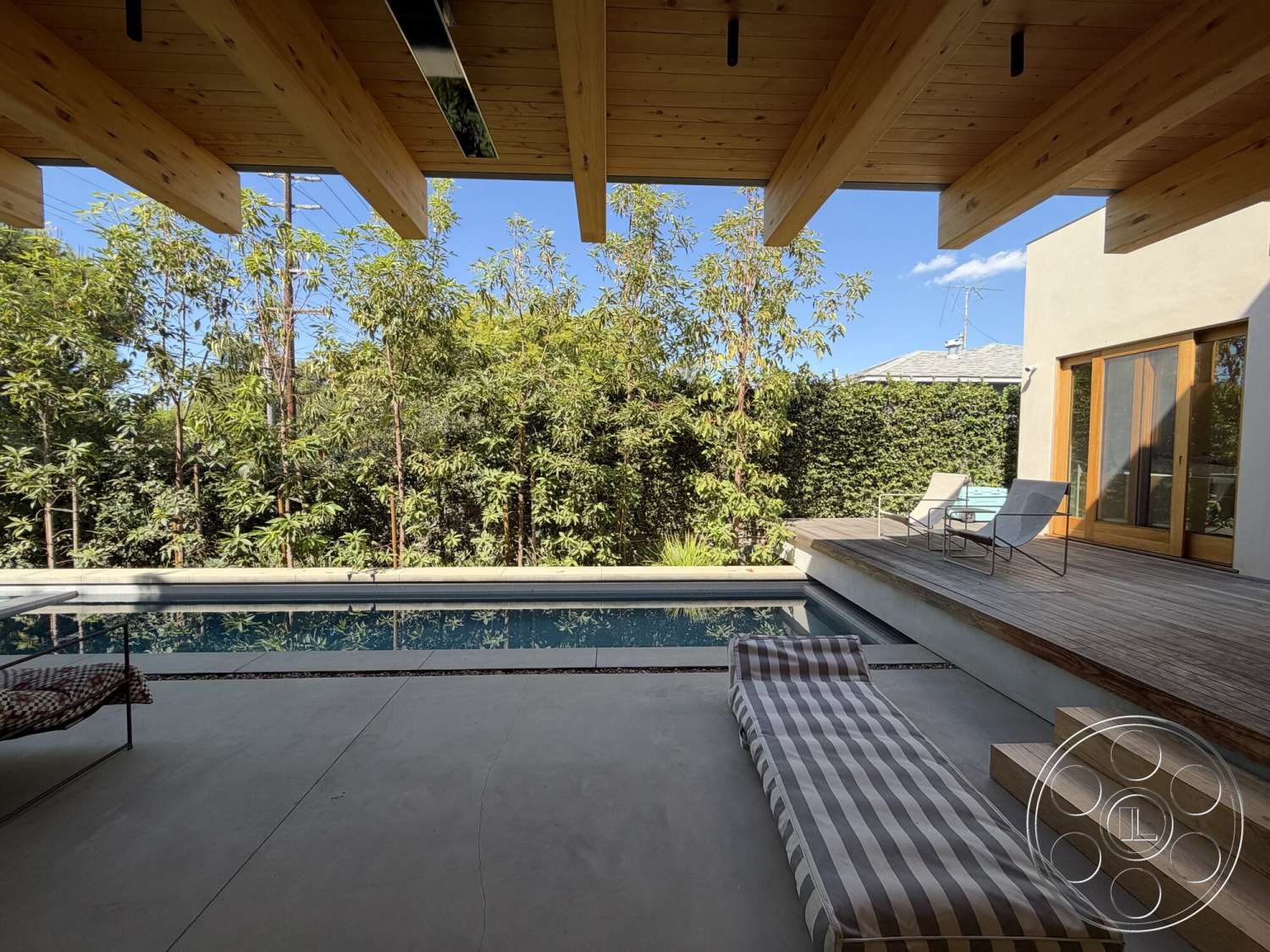 Retro House - exterior, sliding glass doors, modern architectural style, rectangular pool, sunny outdoor setting, wood beam ceiling, wooden deck area, concrete patio floor, lush greenery landscaping, built-in wooden seating