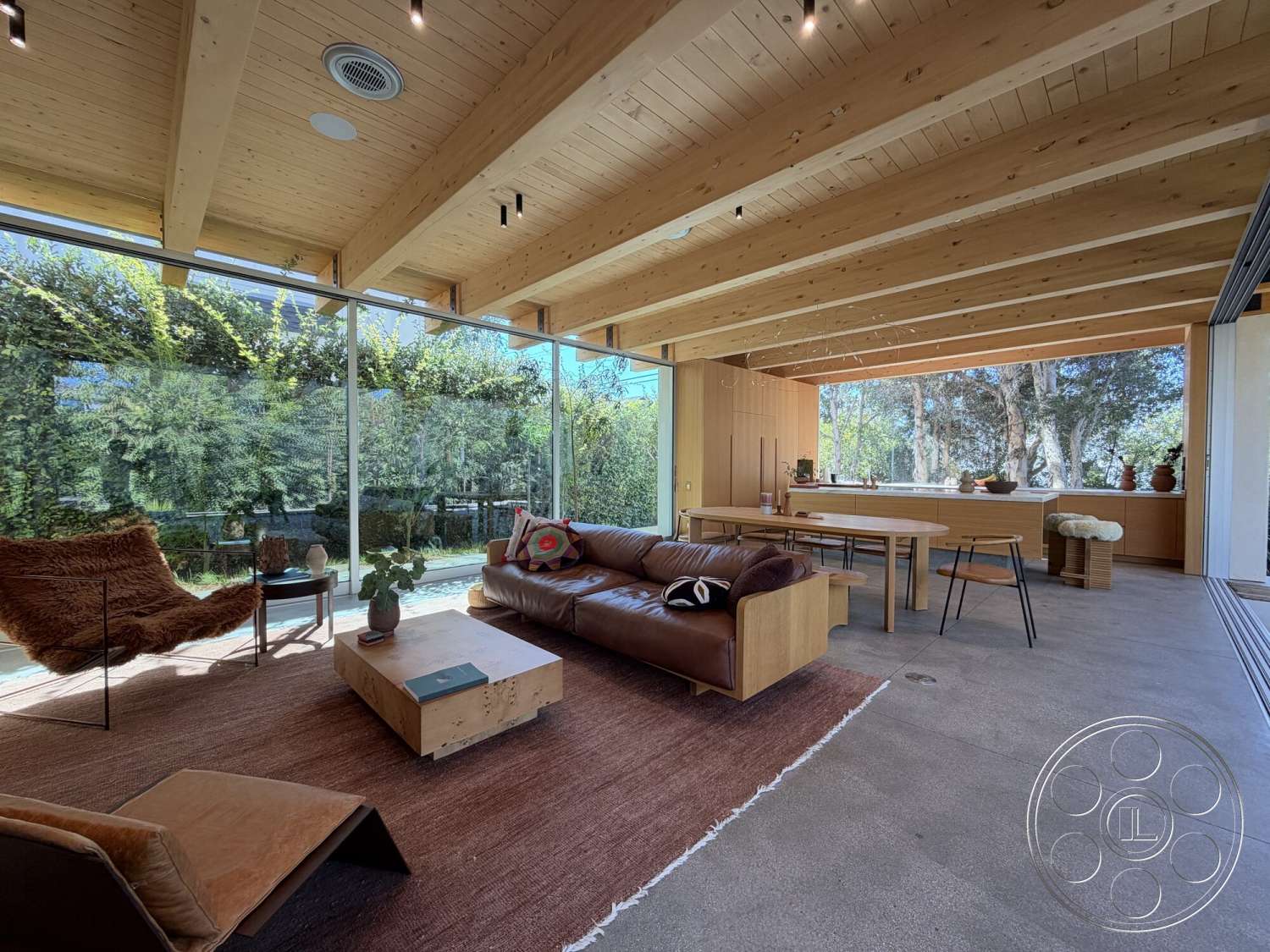 Retro House - concrete flooring, wood dining table, woven area rug, brown leather sofa, contemporary architectural style, exposed wood ceiling beams, minimalist interior design, indoor plants decor, glass wall panels, open floor plan living space, natural light flooding interior, outdoor greenery view, modern kitchen area