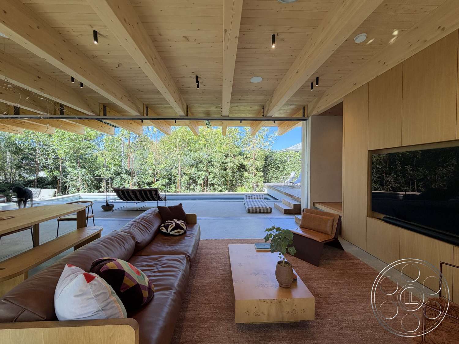 Retro House - neutral color palette, exterior, minimalist design, textured area rug, open floor plan, greenery view, light wood cabinetry, natural wood furniture, rectangular coffee table, brown leather sectional sofa, exposed wood ceiling beams, concrete patio floor, floor-to-ceiling glass doors, urban setting with trees