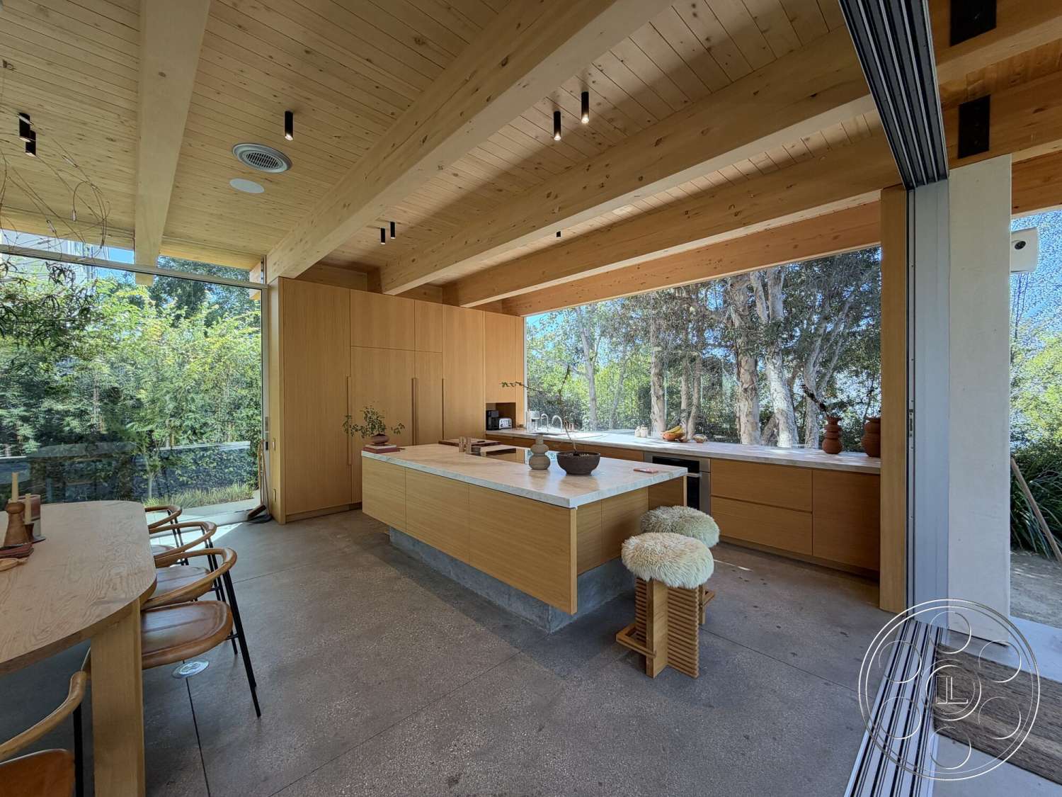 Retro House - natural light, light wood cabinetry, integrated appliances, open-concept layout, modern bar stools, lush greenery view, exposed wood ceiling beams, marble kitchen island countertop, minimalist kitchen design, floor-to-ceiling glass walls, wood plank ceiling, concrete kitchen flooring, decorative ceramic kitchenware