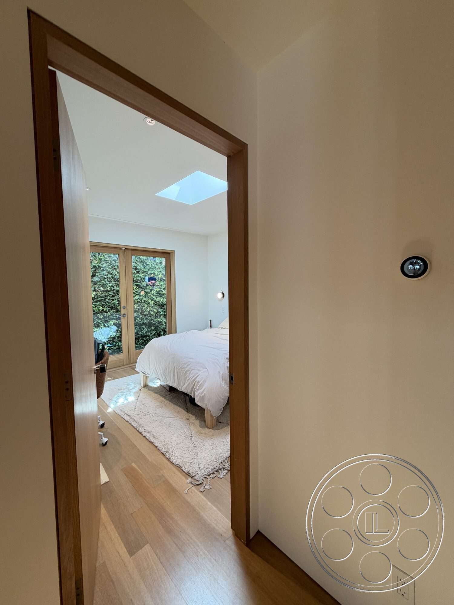 Retro House - minimalist decor, natural light, hardwood flooring, lush greenery view, light area rug, interior bedroom, white painted walls, skylight ceiling, double wooden doors, wood trim door frame