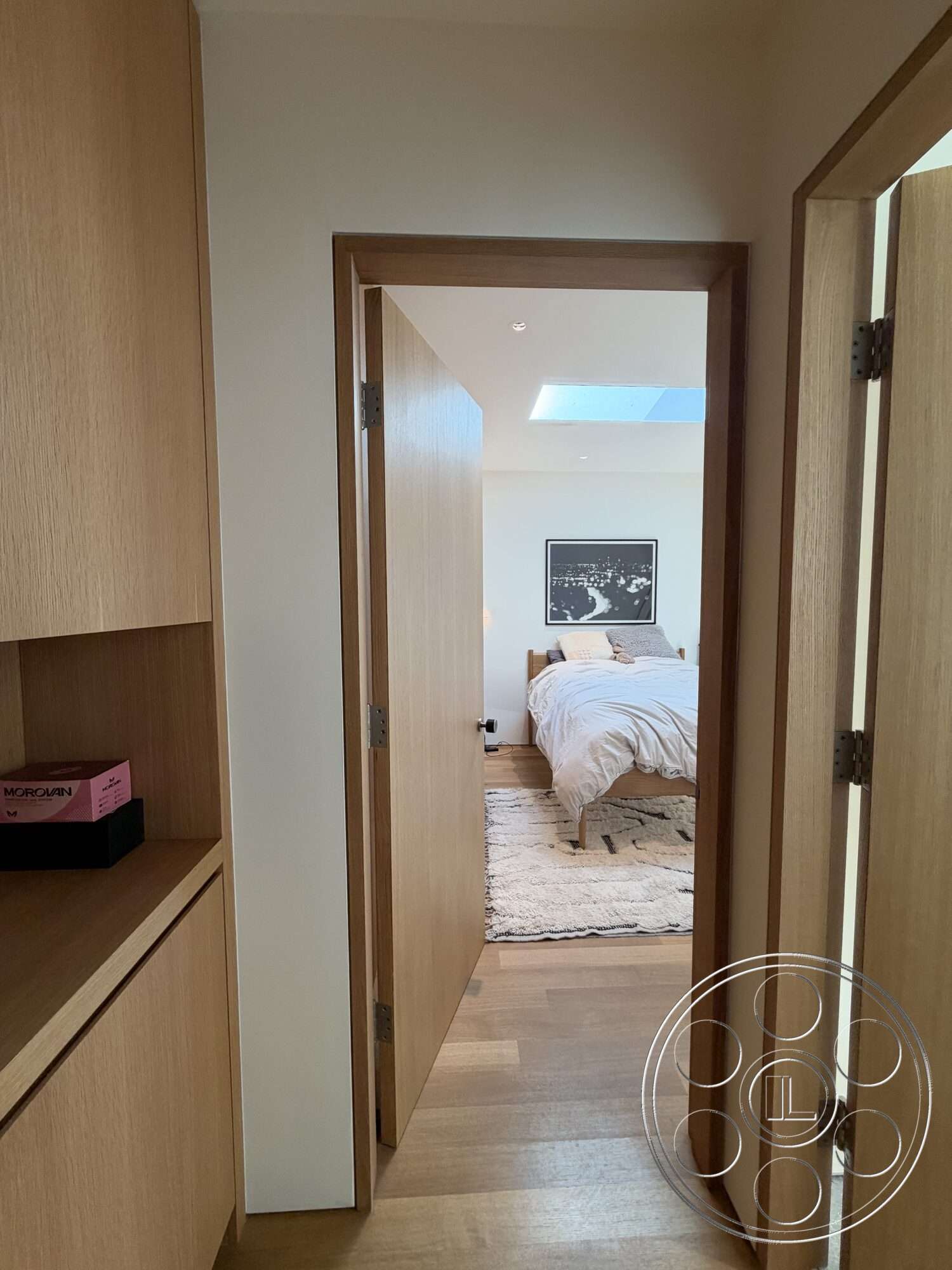 Retro House - hardwood flooring, minimalist design, neutral wall colors, framed artwork, light wood cabinetry, comfortable bedding, wooden bed frame, skylight, open doorway, modern bedroom, natural wood door trim, soft-textured area rug