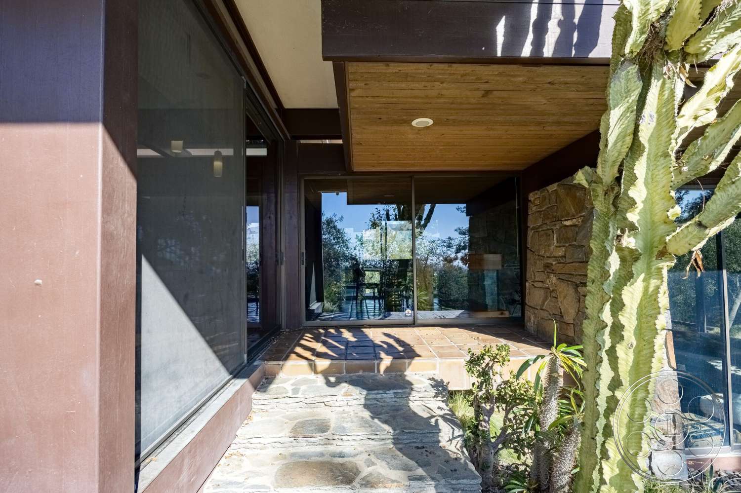 MCM 29 - exterior, wood ceiling, glass sliding doors, floor-to-ceiling windows, modern architectural style, desert landscaping, natural stone steps, brown wooden walls, landscaped garden area, tile entryway flooring