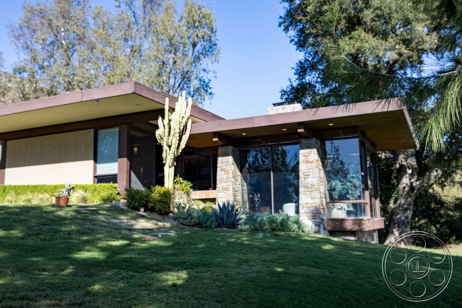 MCM 29 - exterior, natural stone accents, flat roof, large glass windows, surrounding trees, modern architectural style, hillside location, stone feature wall, terraced lawn, horizontal wood siding, lush green landscaping, desert plant landscaping, wood overhang, bushes and succulents