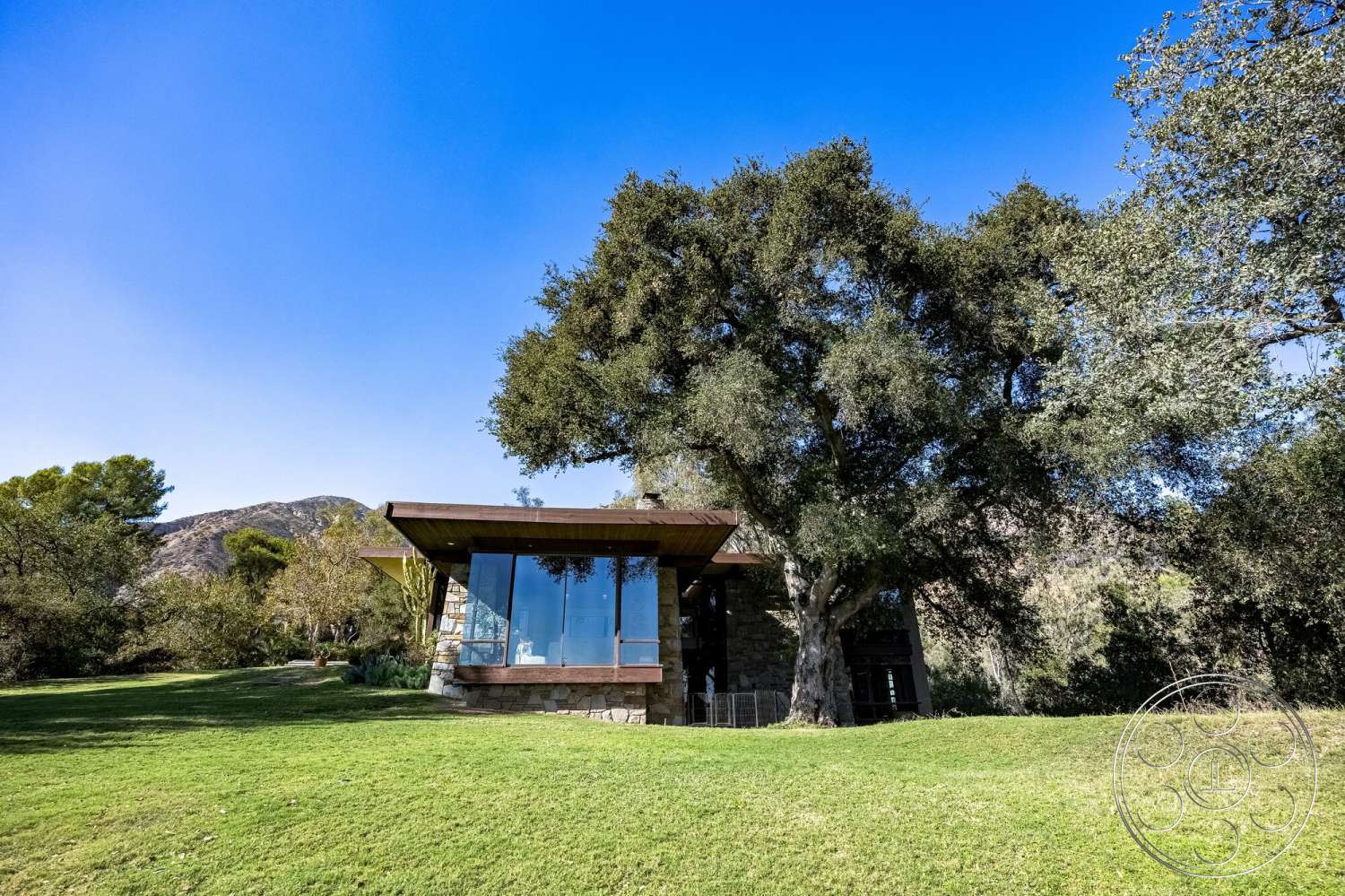 MCM 29 - exterior, modern architecture, large glass windows, open space design, horizontal lines, surrounding trees, mountain view, natural stone walls, integrated with nature, landscaped green lawn, wood roof overhang
