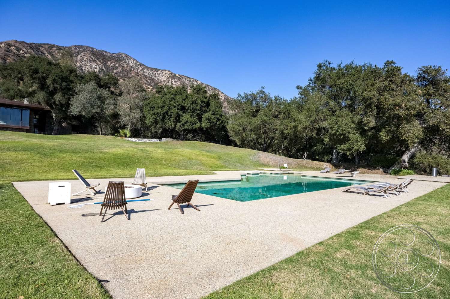 MCM 29 - exterior, landscaped garden, lawn area, mountain backdrop, rectangular pool, wooden lounge chairs, concrete patio flooring, concrete pool border, glass wall of the house