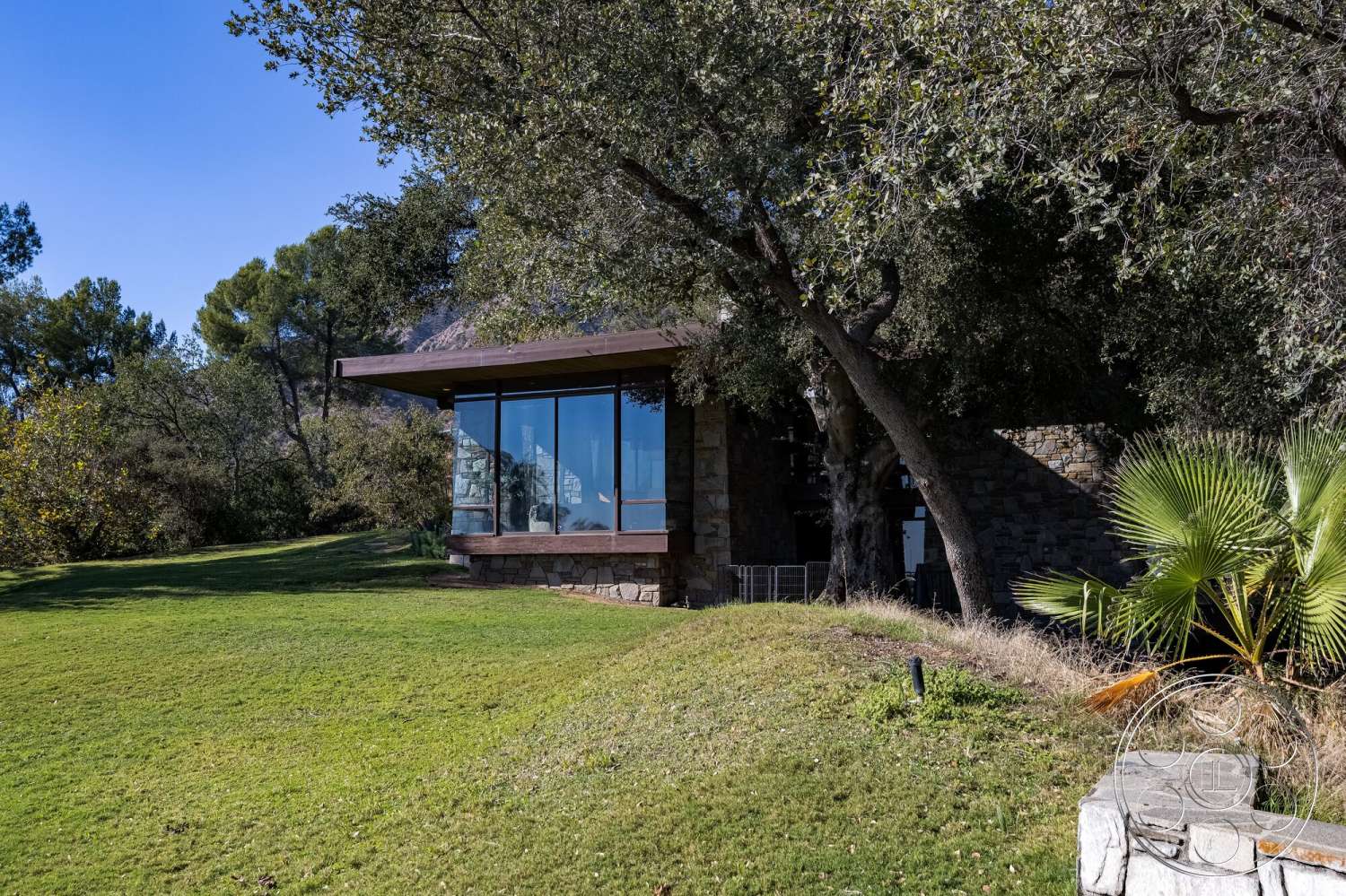 MCM 29 - exterior, surrounding trees, sloping terrain, glass windows, modern architectural style, natural stone walls, landscaped lawn, wood roof, stone foundation