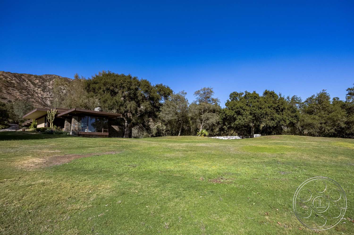 MCM 29 - exterior, landscaped garden, modern architecture, flat roof, large glass windows, green lawn, mountain backdrop, natural stone pathway, desert setting, stone wall accents