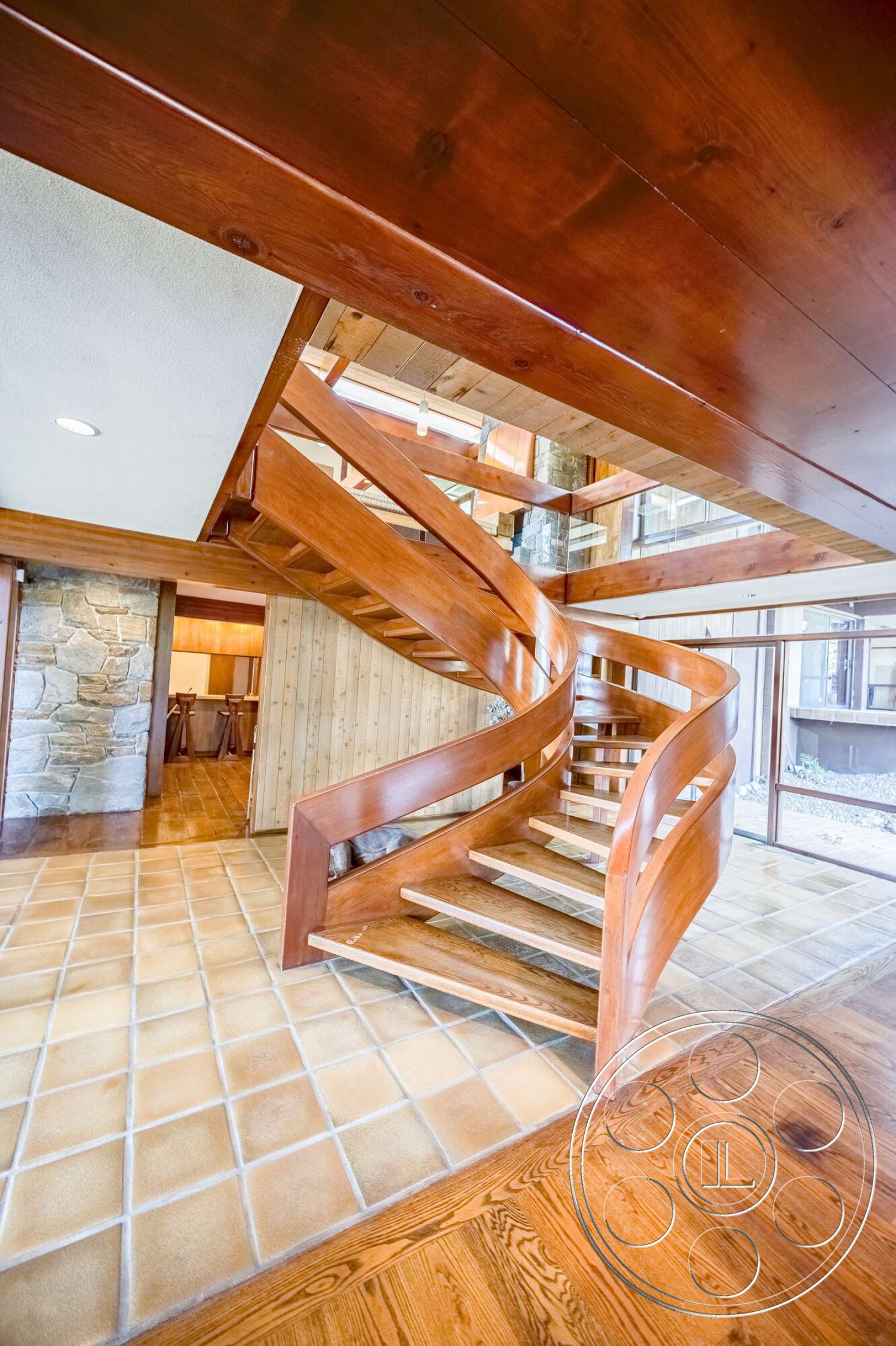 MCM 29 - stone accent wall, open floor plan, wooden staircase, spiral staircase, natural wood paneling, modern home design, wood beam ceiling, stained wood railing, tile entry flooring, beige tile floor, oak hardwood floors