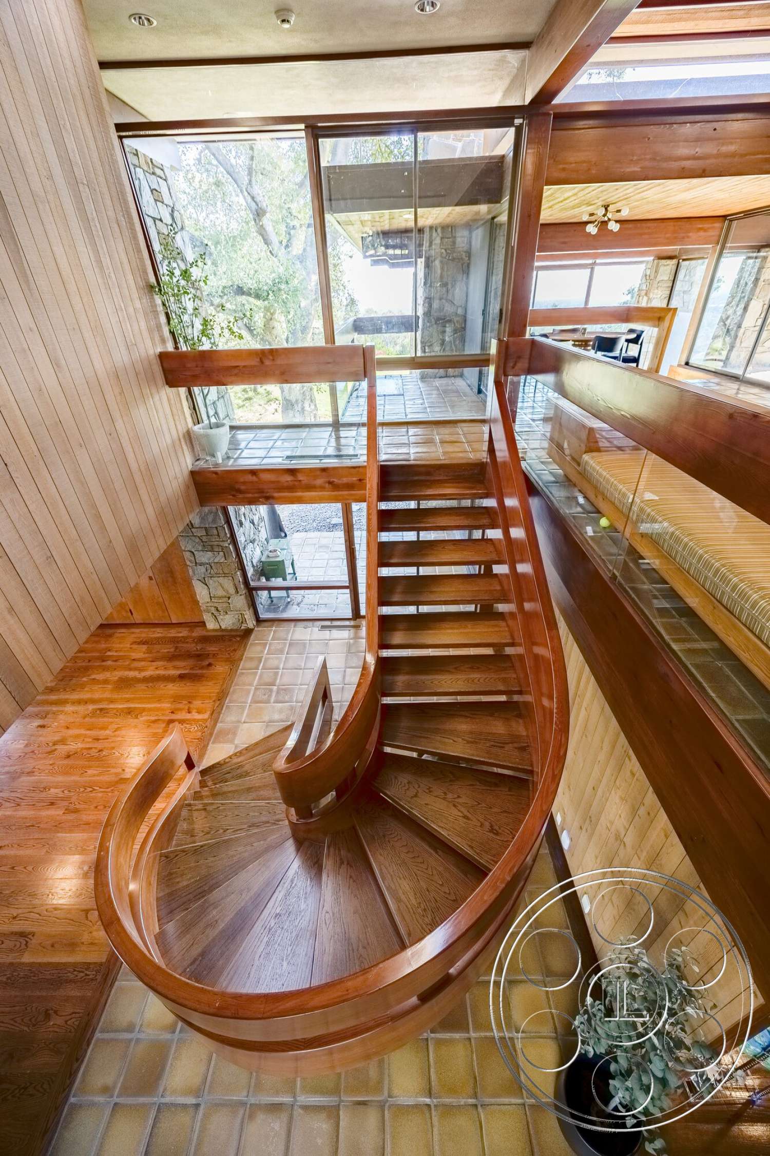 MCM 29 - tile flooring, stone accent wall, light wood flooring, glass railing, vaulted ceiling, modern architectural style, open concept living space, exposed ceiling beams, lush greenery view, recessed lighting fixtures, floor-to-ceiling glass windows, curved wooden staircase, natural wood paneling walls