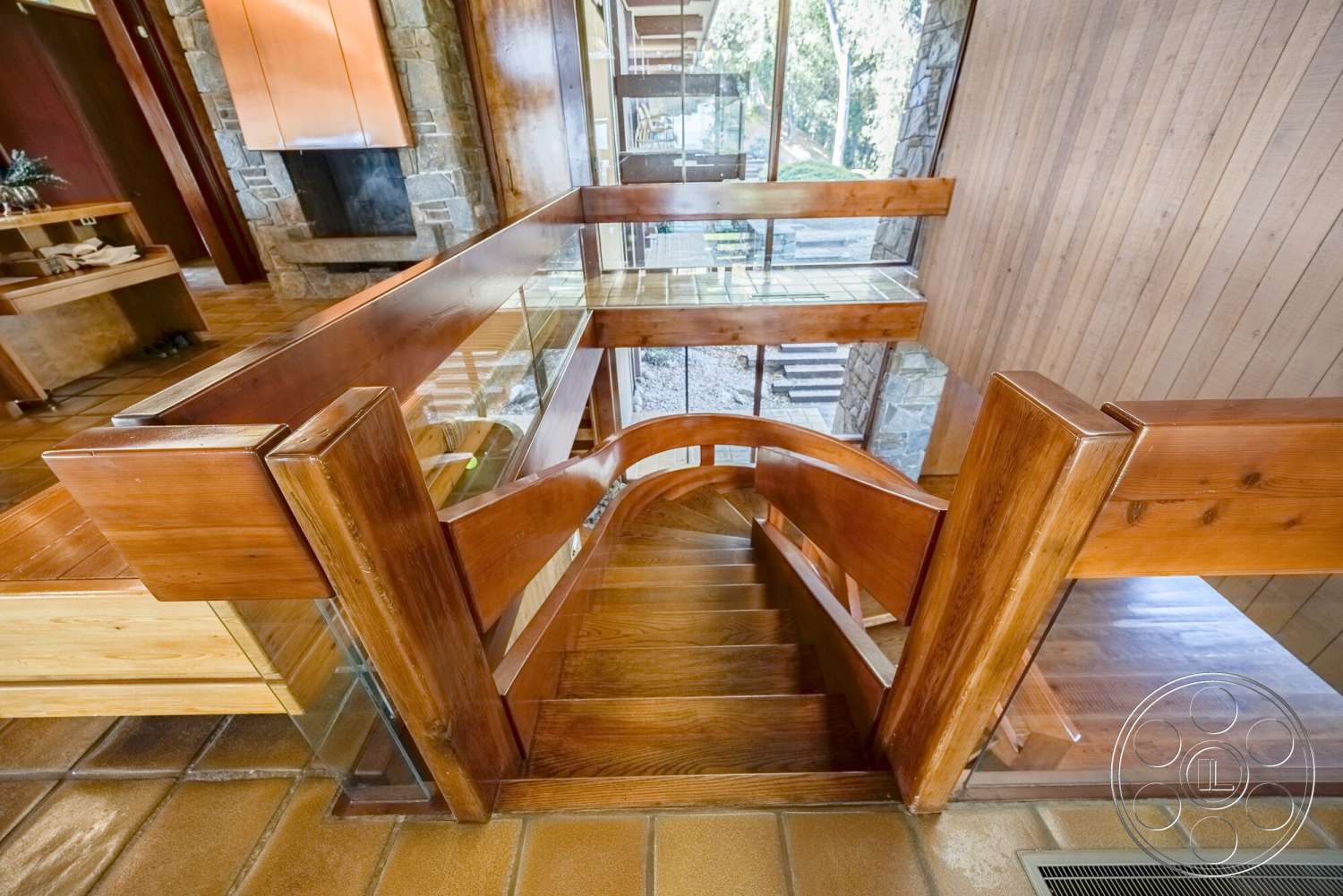 MCM 29 - floor-to-ceiling windows, modern architectural style, warm wood paneling, glass stair railing, stone fireplace wall, exposed wood ceiling, curved wooden staircase, tile entry flooring, polished hardwood railings
