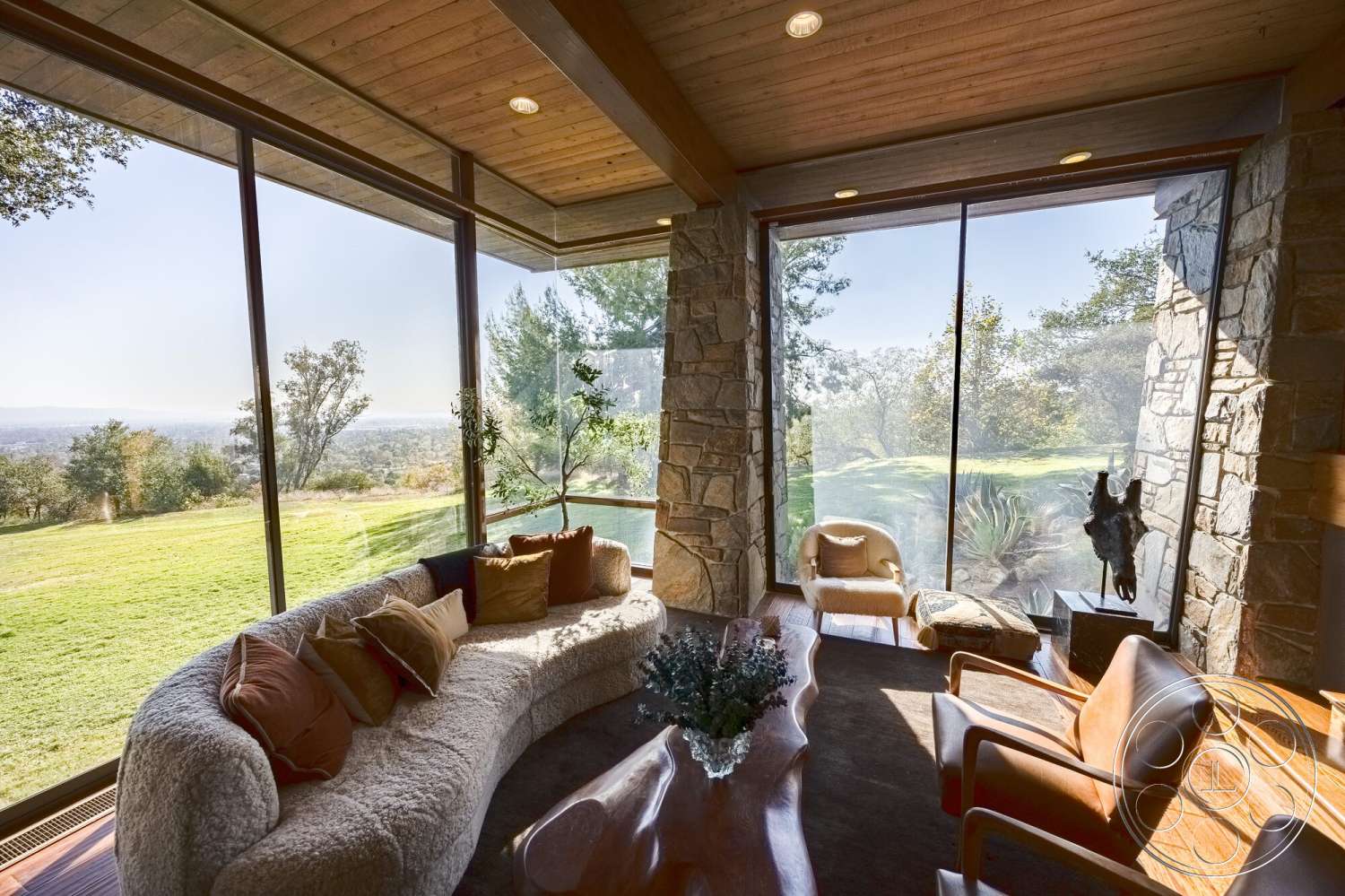 MCM 29 - natural light, minimalist design, textured area rug, wooden coffee table, decorative pillows, green landscape view, hardwood floor, modern lounge area, stone feature wall, curved sectional sofa, wood beam ceiling, floor-to-ceiling glass windows
