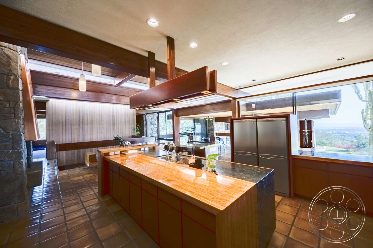 MCM 29 - stone accent wall, wood cabinetry, modern pendant lighting, glass sliding doors, floor-to-ceiling windows, large kitchen island, granite kitchen countertops, open-concept kitchen design, natural light ambiance, panoramic mountain view, hardwood ceiling beams, slate kitchen flooring