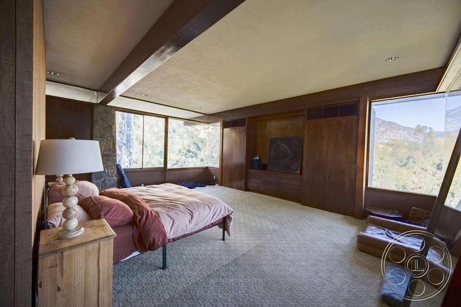 MCM 29 - stone accent wall, wood paneling, floor-to-ceiling windows, mountain view, textured plaster walls, modern artwork, wood nightstand, exposed wood ceiling beams, carpet bedroom flooring, lampshade lamp