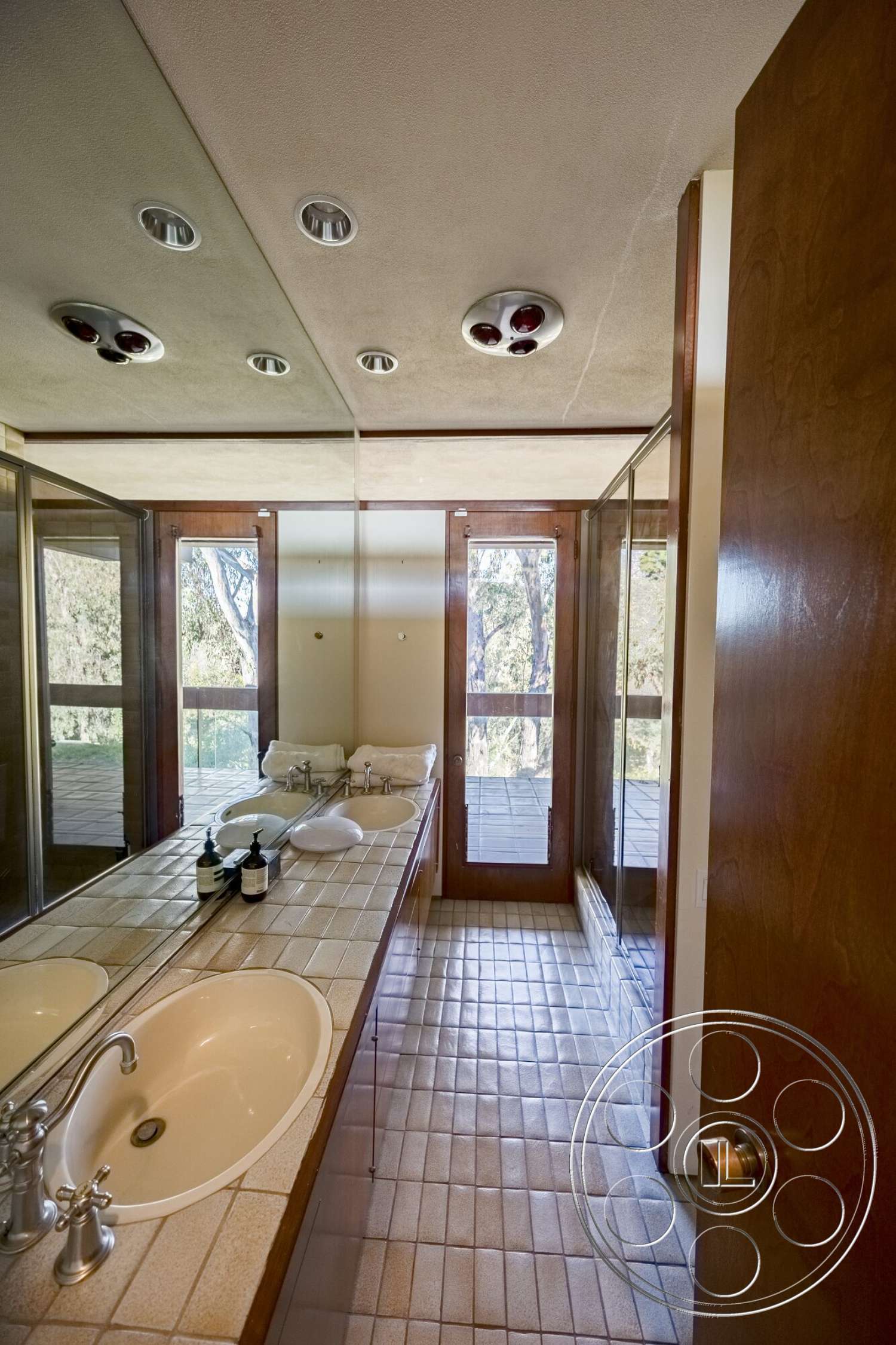 MCM 29 - wood cabinetry, glass shower enclosure, neutral wall color, mirrored wall, double door entry, recessed ceiling lights, modern bathroom design, tile bathroom flooring, floating vanities with dual sinks, plenty of natural light