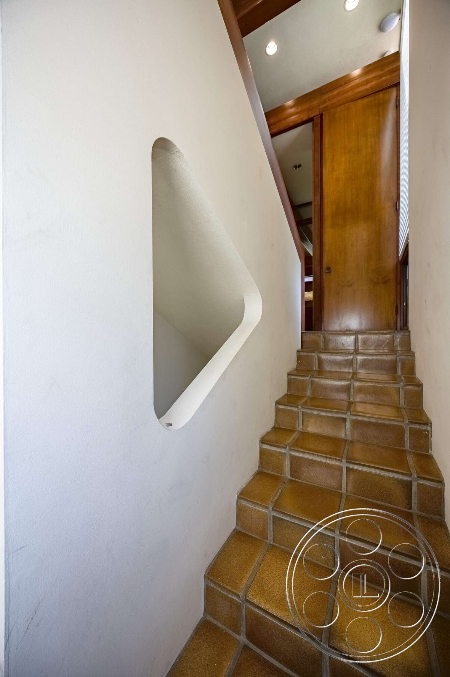 MCM 29 - modern architectural style, textured plaster walls, built-in lighting, smooth ceiling, rectangular staircase, stained wood door, medium wood trim, tan tile staircase, cut-out wall opening