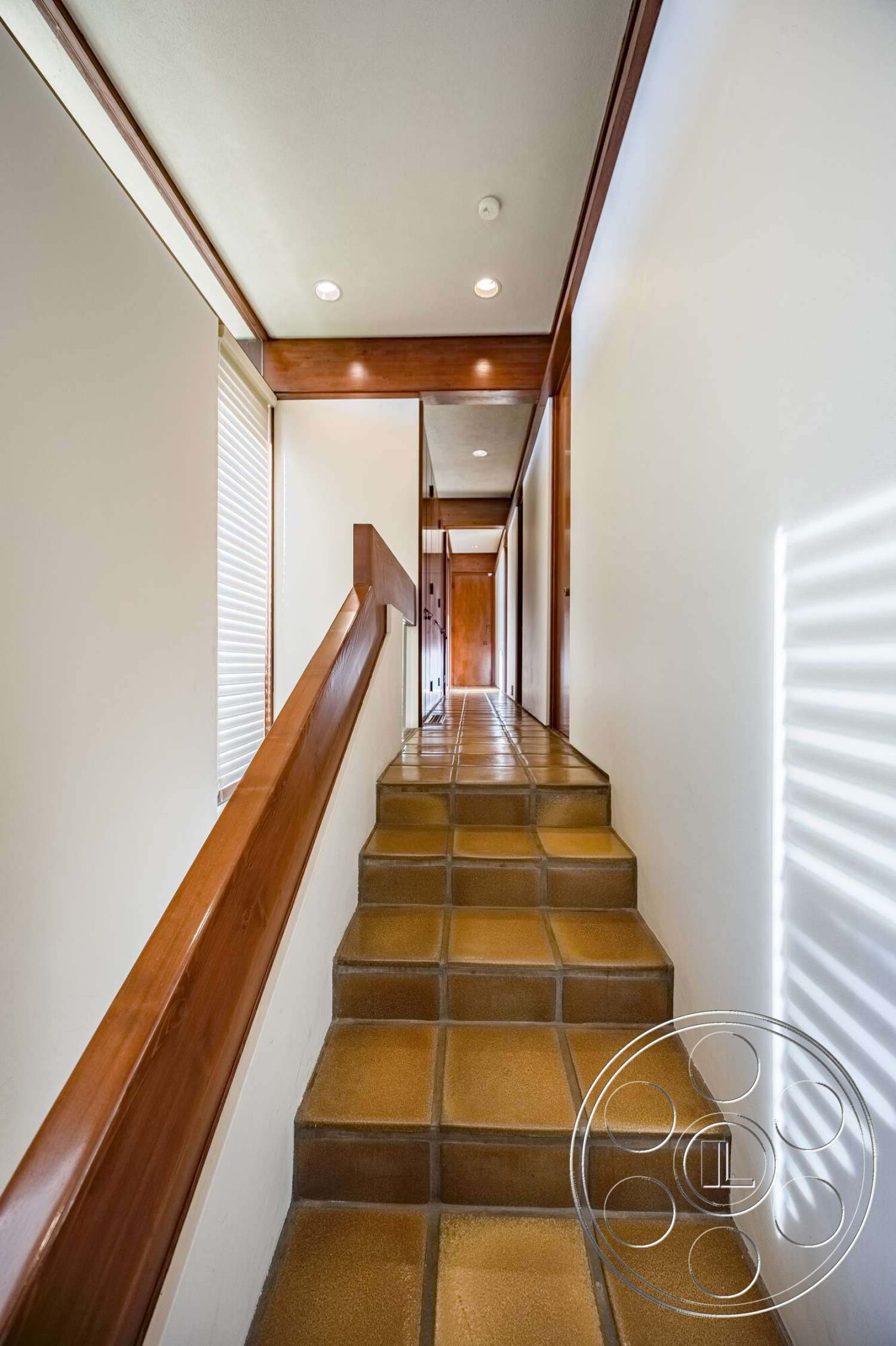 MCM 29 - open hallway, textured plaster walls, natural light from windows, recessed lighting fixtures, spacious corridor layout, wood handrail, ceramic tile staircase, warm wood trim details