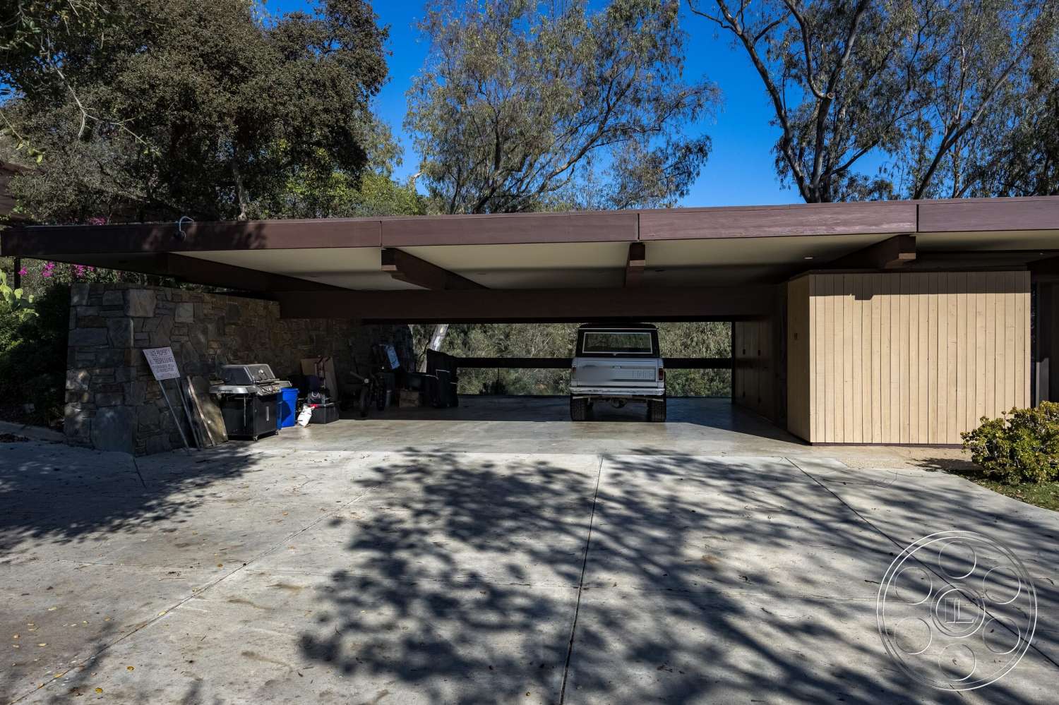 MCM 29 - natural light, exterior, stone accent wall, modern architectural style, concrete driveway, flat roof overhang, open carport, outdoor grilling area, vegetation landscaping, wood panel carport ceiling