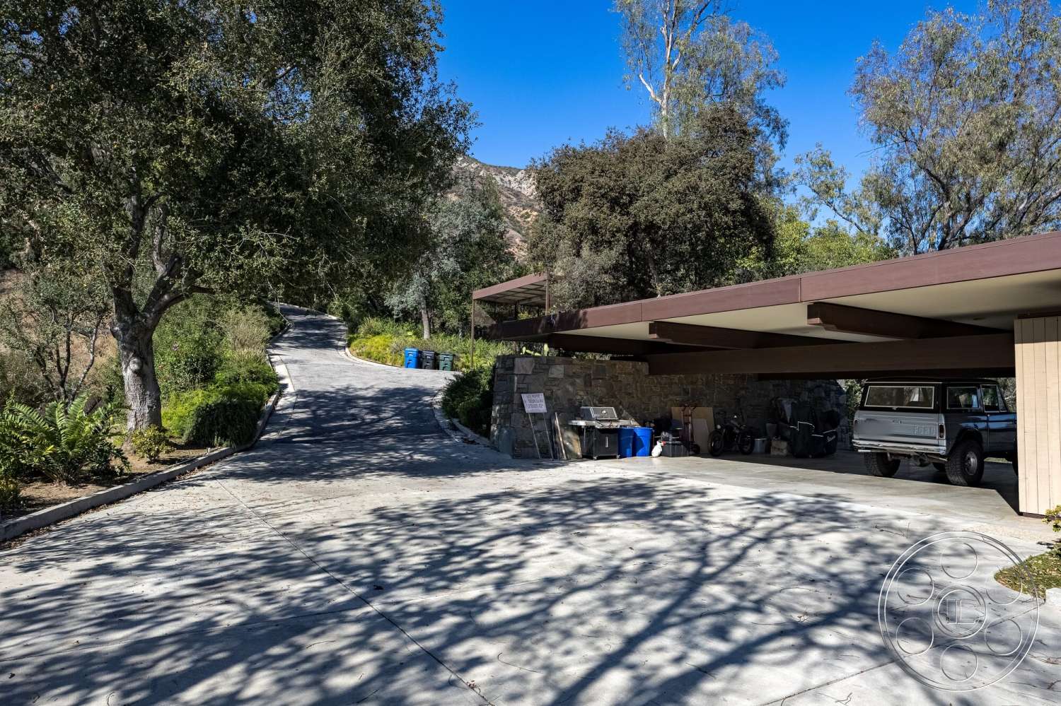 MCM 29 - exterior, stone wall, wood paneling, green landscaping, mountain view, concrete driveway, curved driveway, overhang roof, natural landscape setting, carport with exposed beams