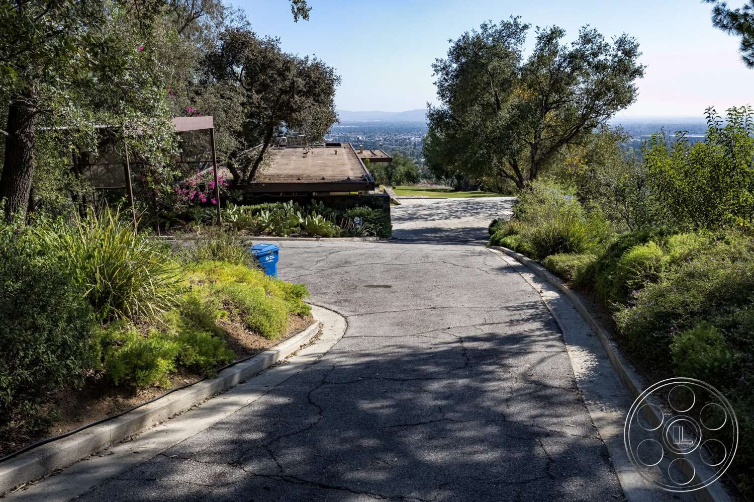 MCM 29 - exterior, single-story home, curved driveway, asphalt driveway, landscaped garden beds, native shrub plantings, stone retaining walls, panoramic hillside view, natural hillside setting, wooden roofing materials
