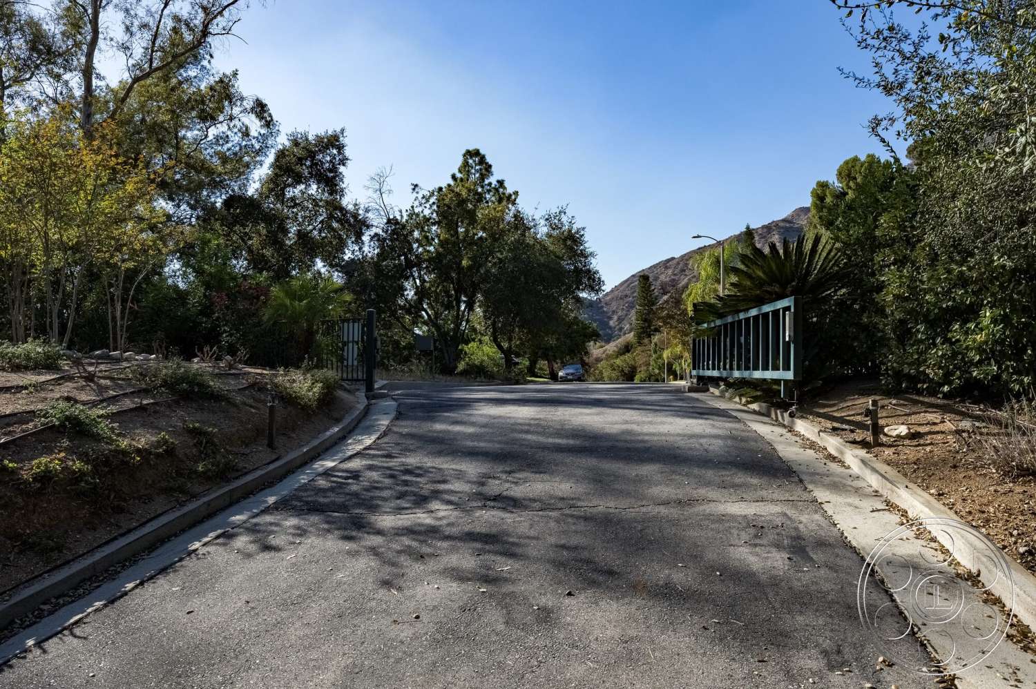 MCM 29 - exterior, surrounding greenery, curved driveway, mountain backdrop, asphalt driveway, suburban environment, natural terrain, landscaped pathway, iron gate entry