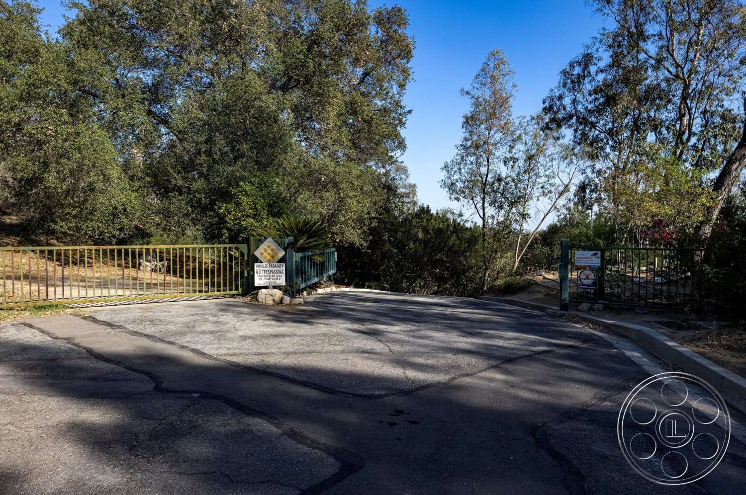 MCM 29 - surrounding trees, natural landscape, clear blue sky, asphalt driveway, rural setting, hillside location, stone gate pillars, yellow metal fencing, aggregate concrete surface, private property entrance