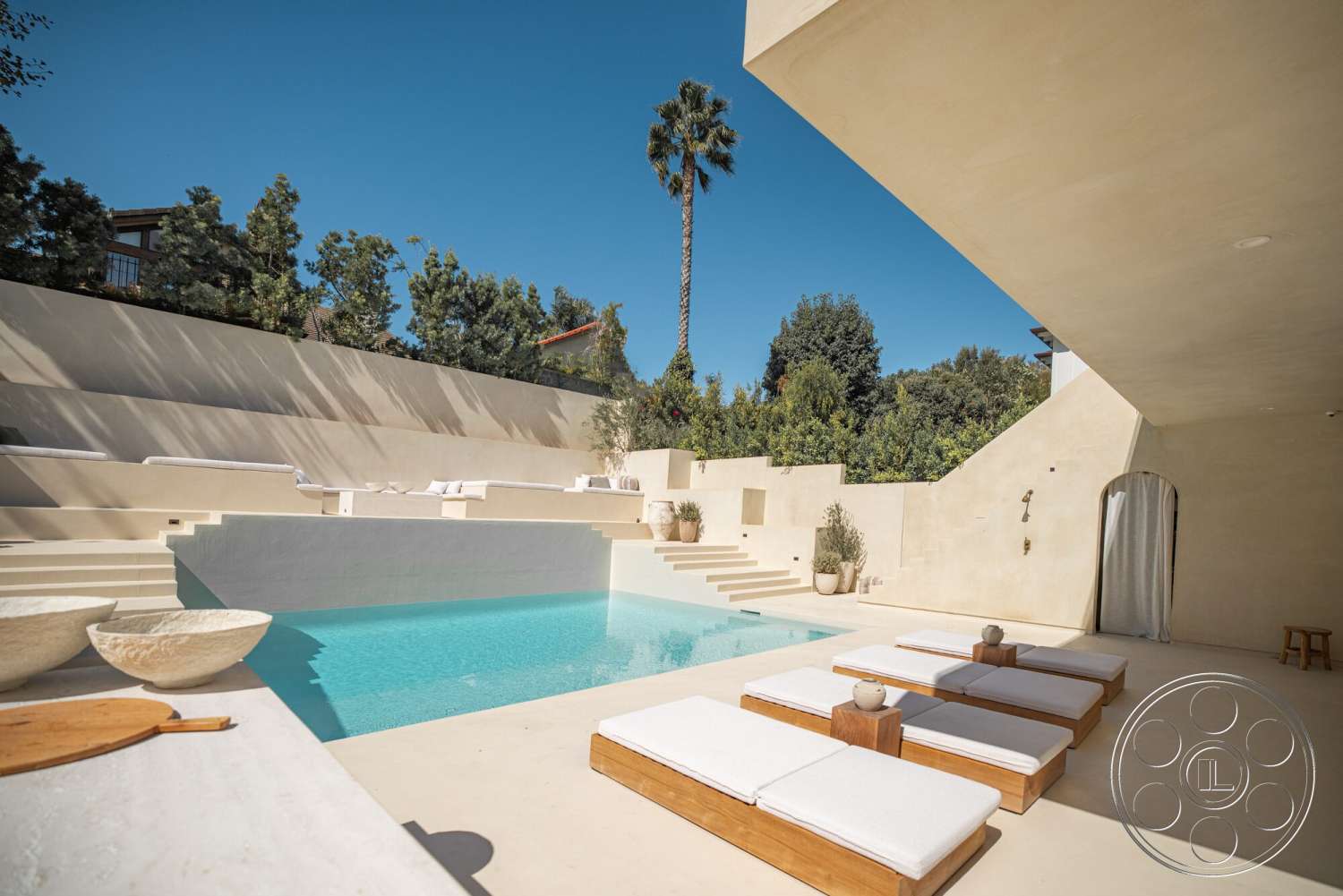 Modern 535 - exterior, rectangular swimming pool, concrete steps, outdoor lounge area, potted greenery, concrete pool deck, landscaped garden area, stucco wall finish, curved seating area, clear blue sky view, wooden sun loungers, palm tree backdrop, stone decorative bowls