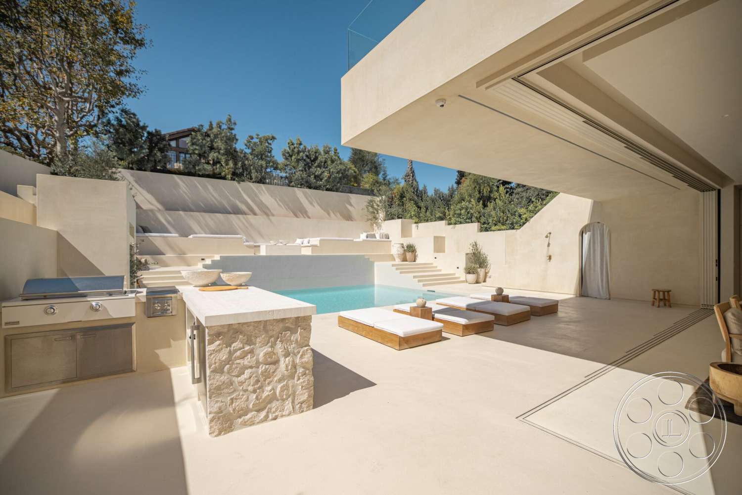 Modern 535 - exterior, built-in outdoor grill, rectangular pool, exposed stone wall, concrete patio flooring, concrete pool border, floor-to-ceiling sliding glass doors, minimalist architectural style, modern outdoor lounge chairs, natural stone outdoor kitchen, landscape with lush greenery, large cantilevered roof overhang, sunny open space, steps leading to the pool area