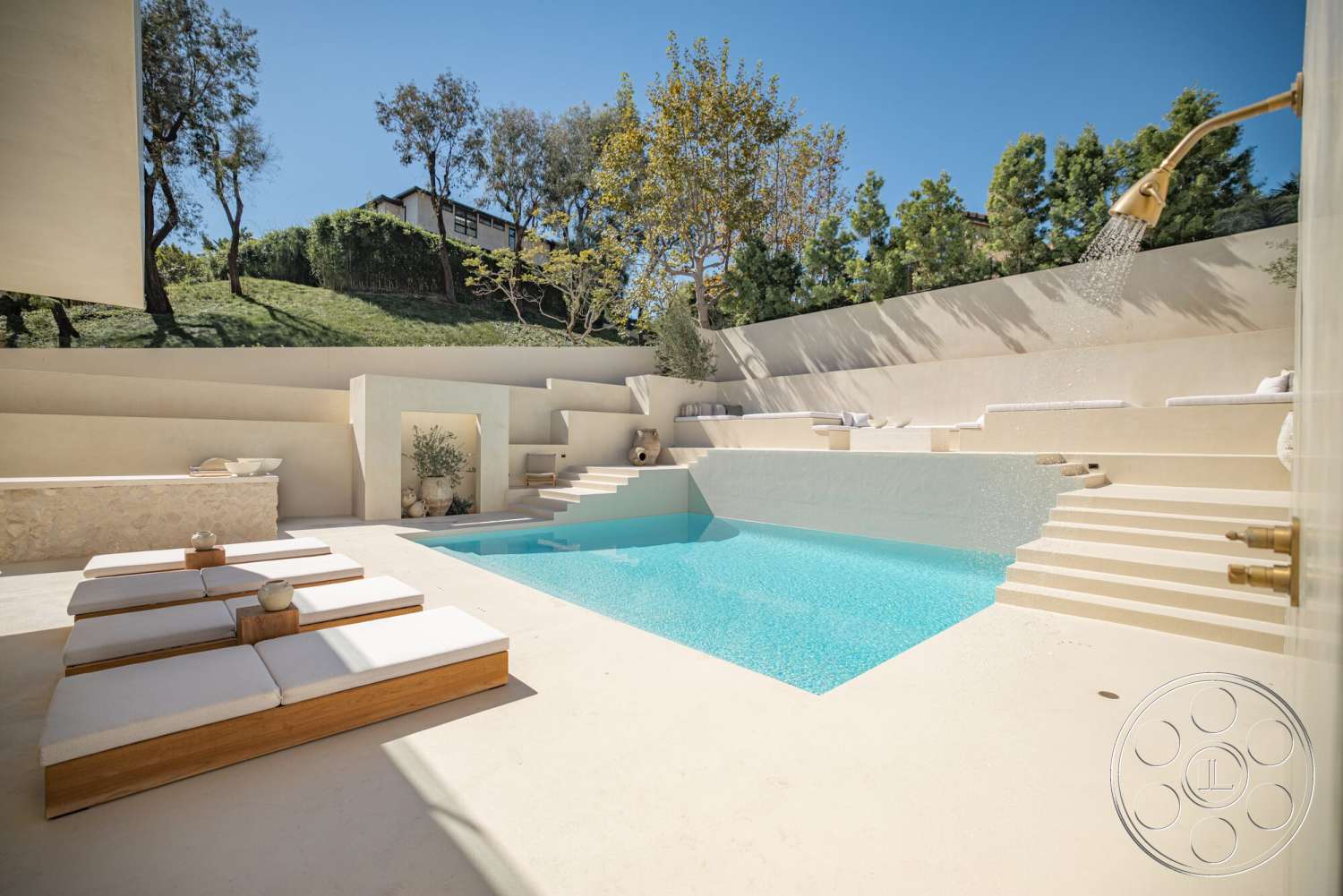 Modern 535 - rectangular swimming pool, concrete pool deck, concrete steps leading to pool, modern outdoor seating area, exterior pool area, sunny hillside location, textured stone wall feature, minimalist sun loungers with wood frames, landscaped yard with grass and trees, outdoor shower with brass fixtures, white stucco retaining walls
