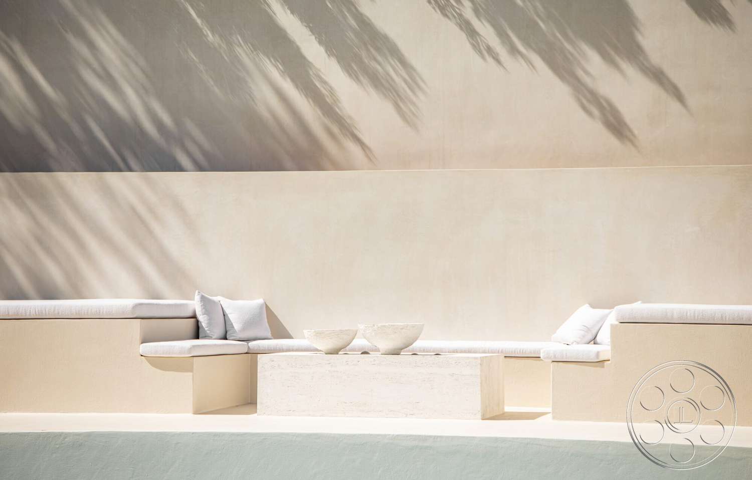 Modern 535 - exterior, textured beige wall, stucco wall finish, simple geometric forms, concrete floor base, concrete bench seating, minimalist outdoor lounge area, natural light shadows, rectangular stone coffee table, light-colored fabric cushions