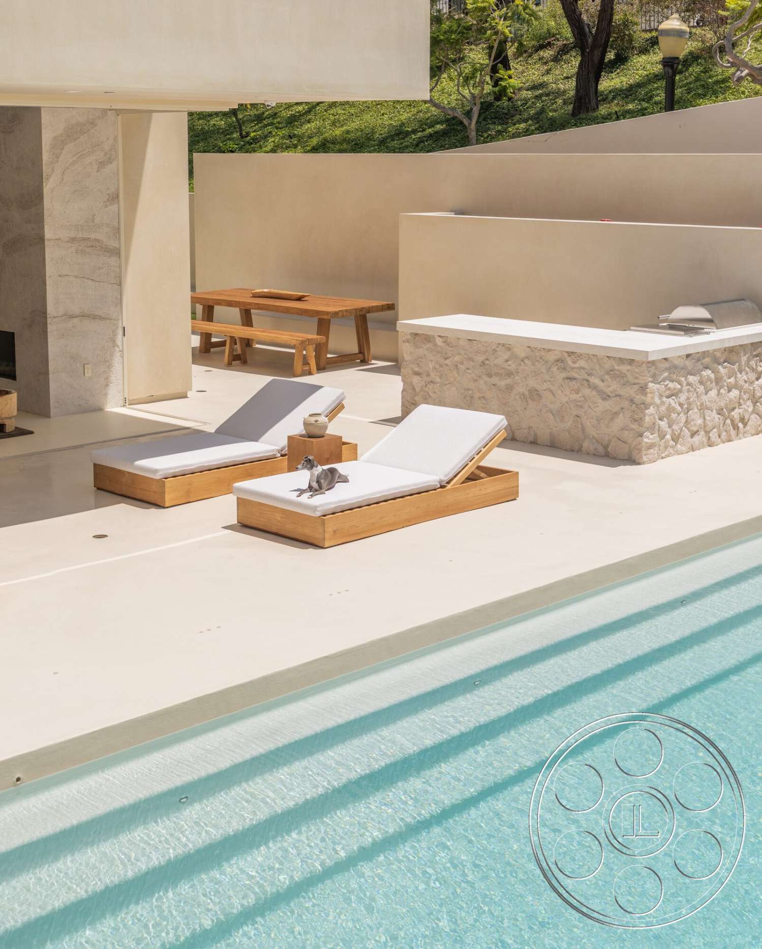 Modern 535 - exterior, rectangular swimming pool, textured plaster walls, stone feature wall, concrete pool border, concrete patio floor, stone outdoor kitchen counter, minimalist outdoor dining area, landscaped greenery background, wooden outdoor loungers