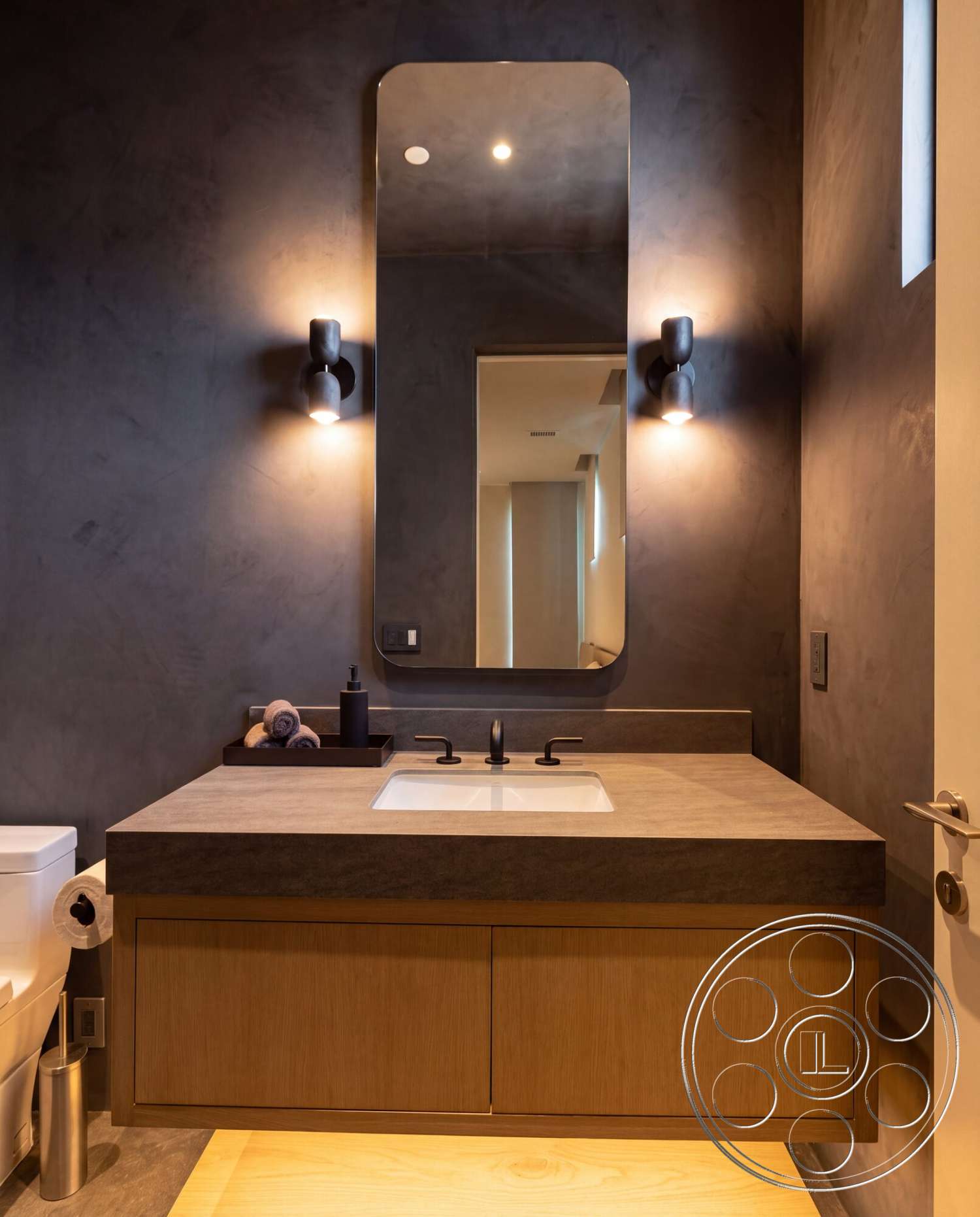 Modern 535 - light wood flooring, oval mirror, minimalist bathroom design, modern wall sconces, textured plaster bathroom walls, wood bathroom vanity, polished concrete countertop, black matte faucet fixtures, floating sink design